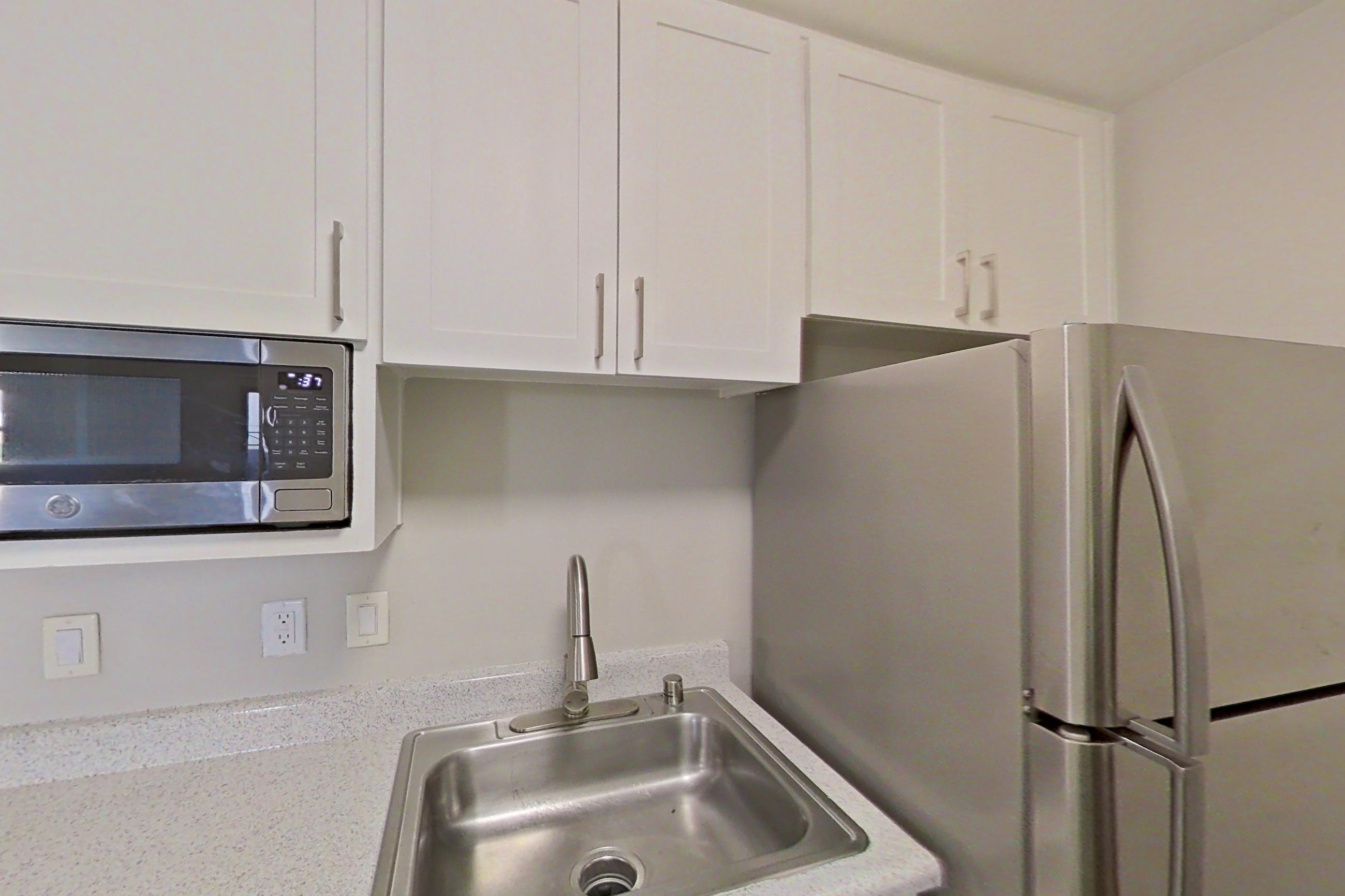 Kitchen with black appliances, dishwasher, light countertops, light stone countertops, light wood-finish flooring, oven/range, refrigerator, and stainless steel appliances, Apartment 12-06 at Avana Rancho Cucamonga