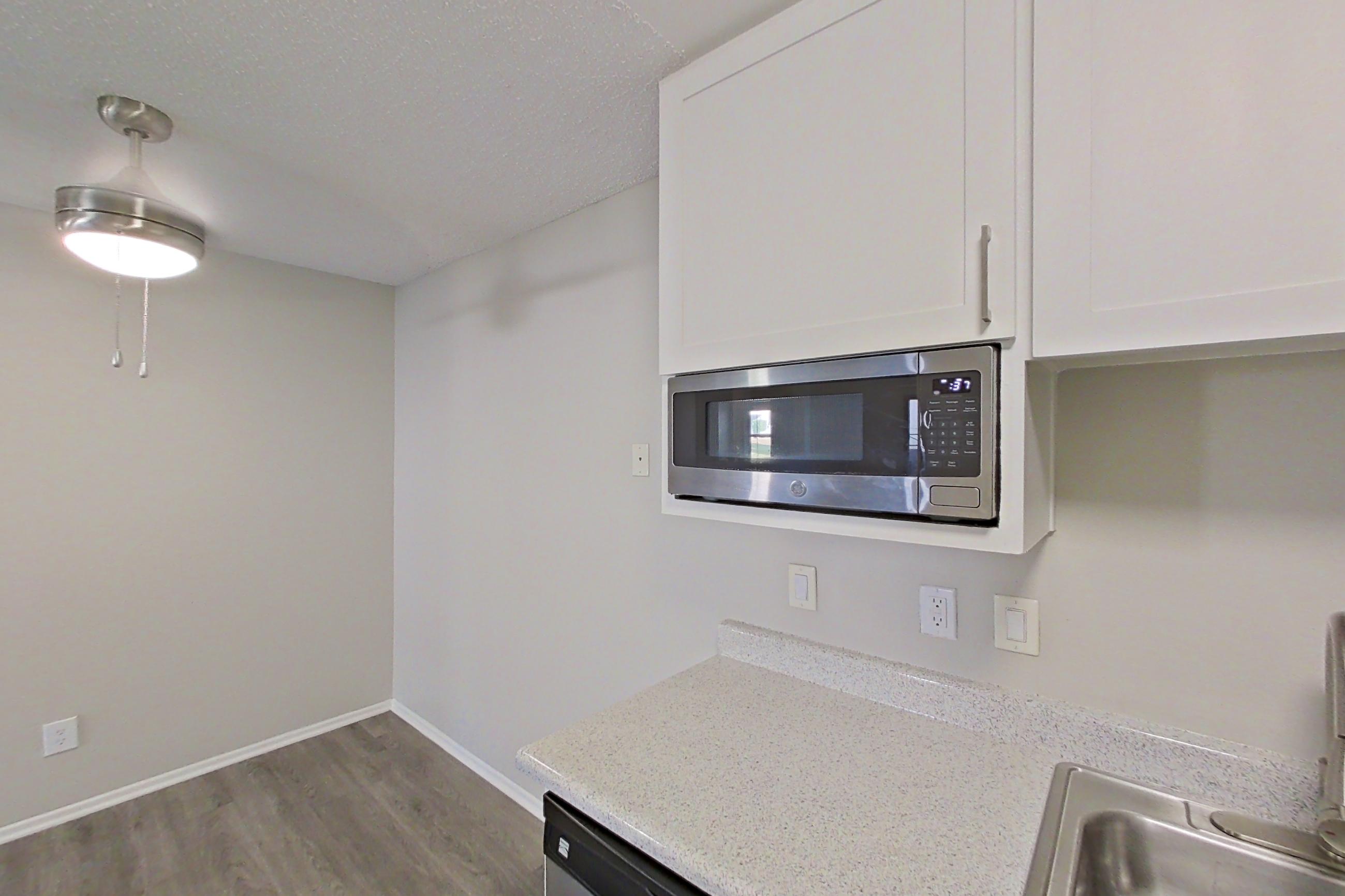 Kitchen with black appliances, dishwasher, light countertops, light stone countertops, light wood-finish flooring, oven/range, refrigerator, and stainless steel appliances, Apartment 12-06 at Avana Rancho Cucamonga