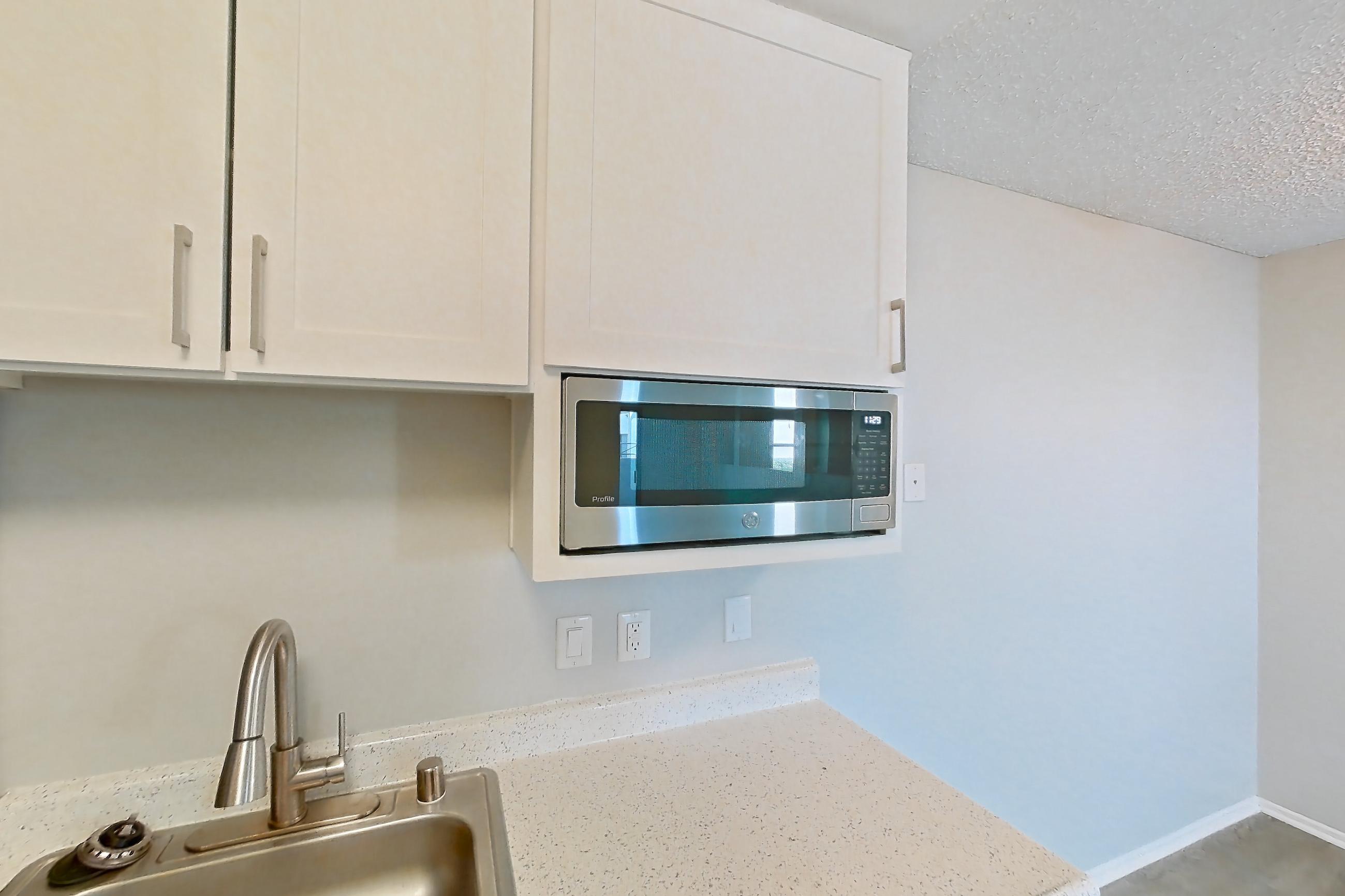 Kitchen with dark wood-finish flooring, dishwasher, light countertops, light stone countertops, light wood-finish flooring, microwave, refrigerator, and stainless steel appliances, Apartment 12-08 at Avana Rancho Cucamonga
