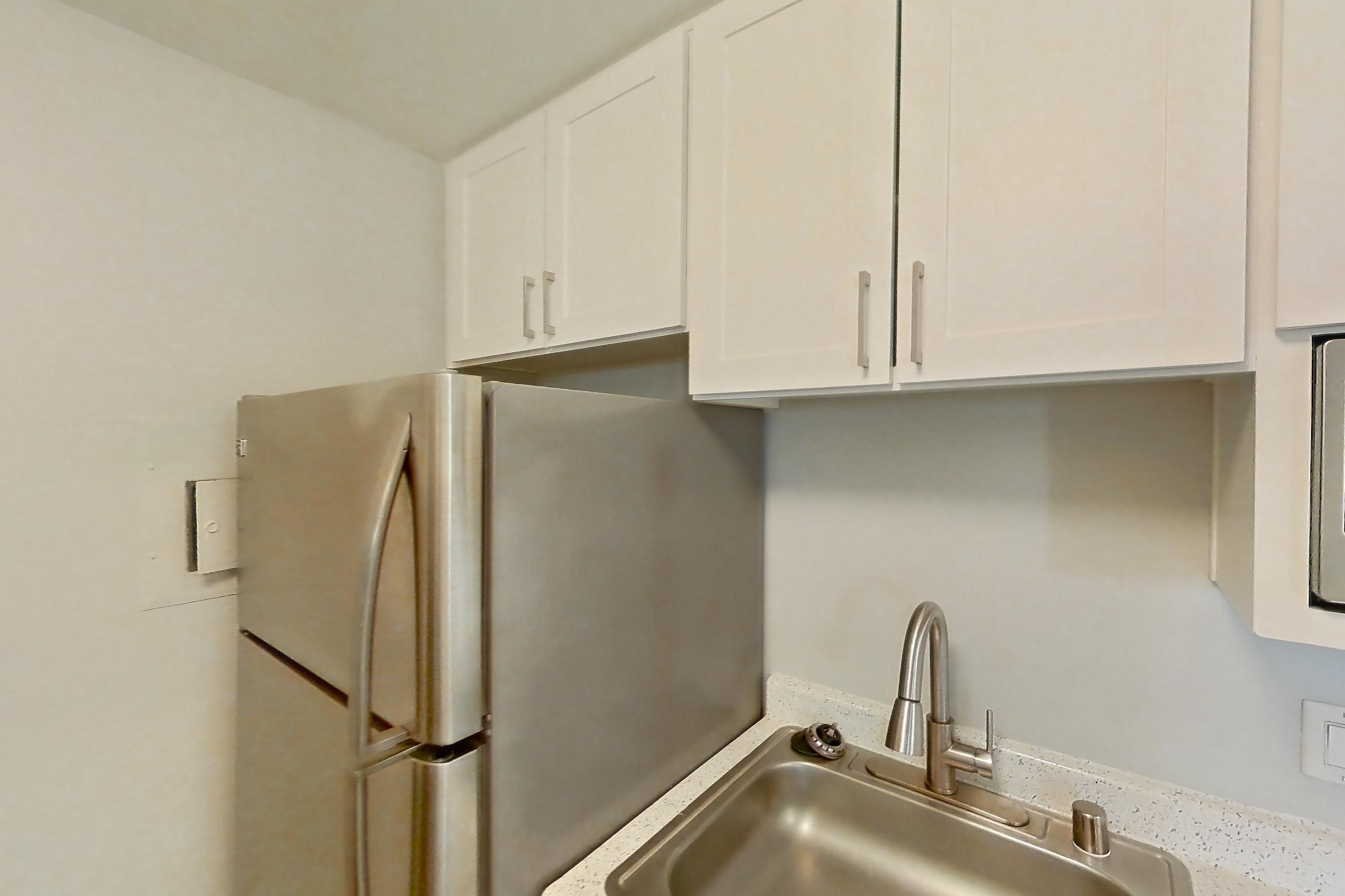 Kitchen with dark wood-finish flooring, dishwasher, light countertops, light stone countertops, light wood-finish flooring, microwave, refrigerator, and stainless steel appliances, Apartment 12-08 at Avana Rancho Cucamonga