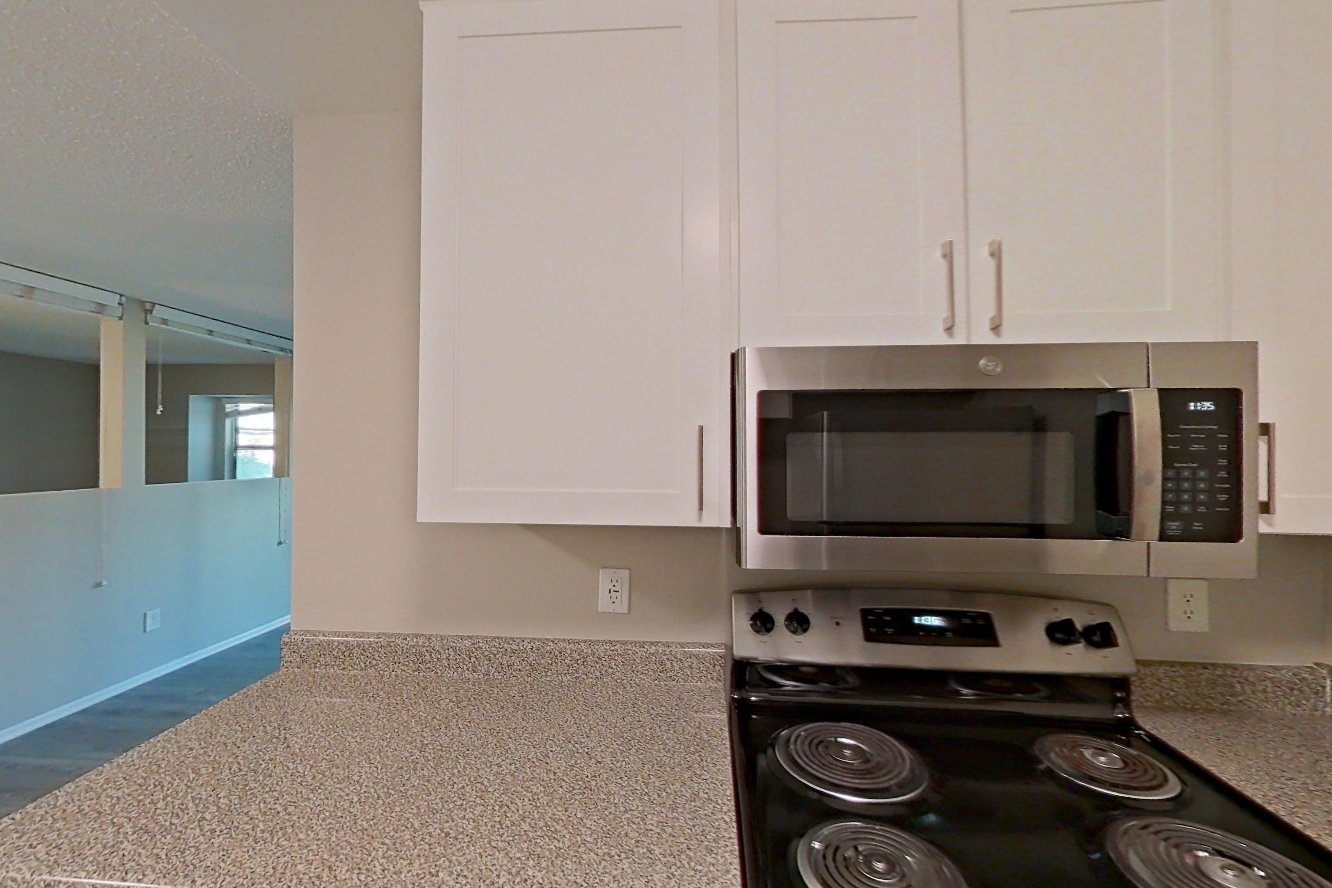 Kitchen with dishwasher, electric range, light countertops, light stone countertops, light wood-finish flooring, microwave, oven/range, and stainless steel appliances, Apartment 13-04 at Avana Rancho Cucamonga