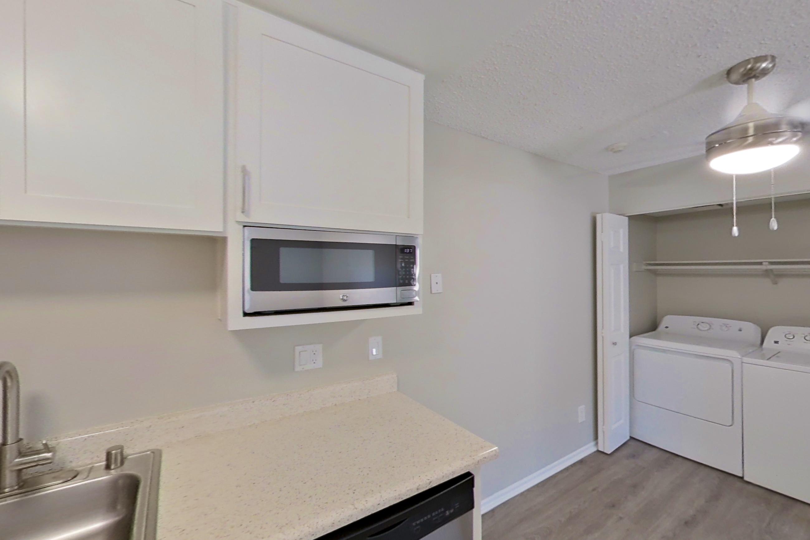 Kitchen with dishwasher, electric range, light countertops, light stone countertops, light wood-finish flooring, microwave, oven/range, refrigerator, stainless steel appliances, and white appliances, Apartment 14-02 at Avana Rancho Cucamonga