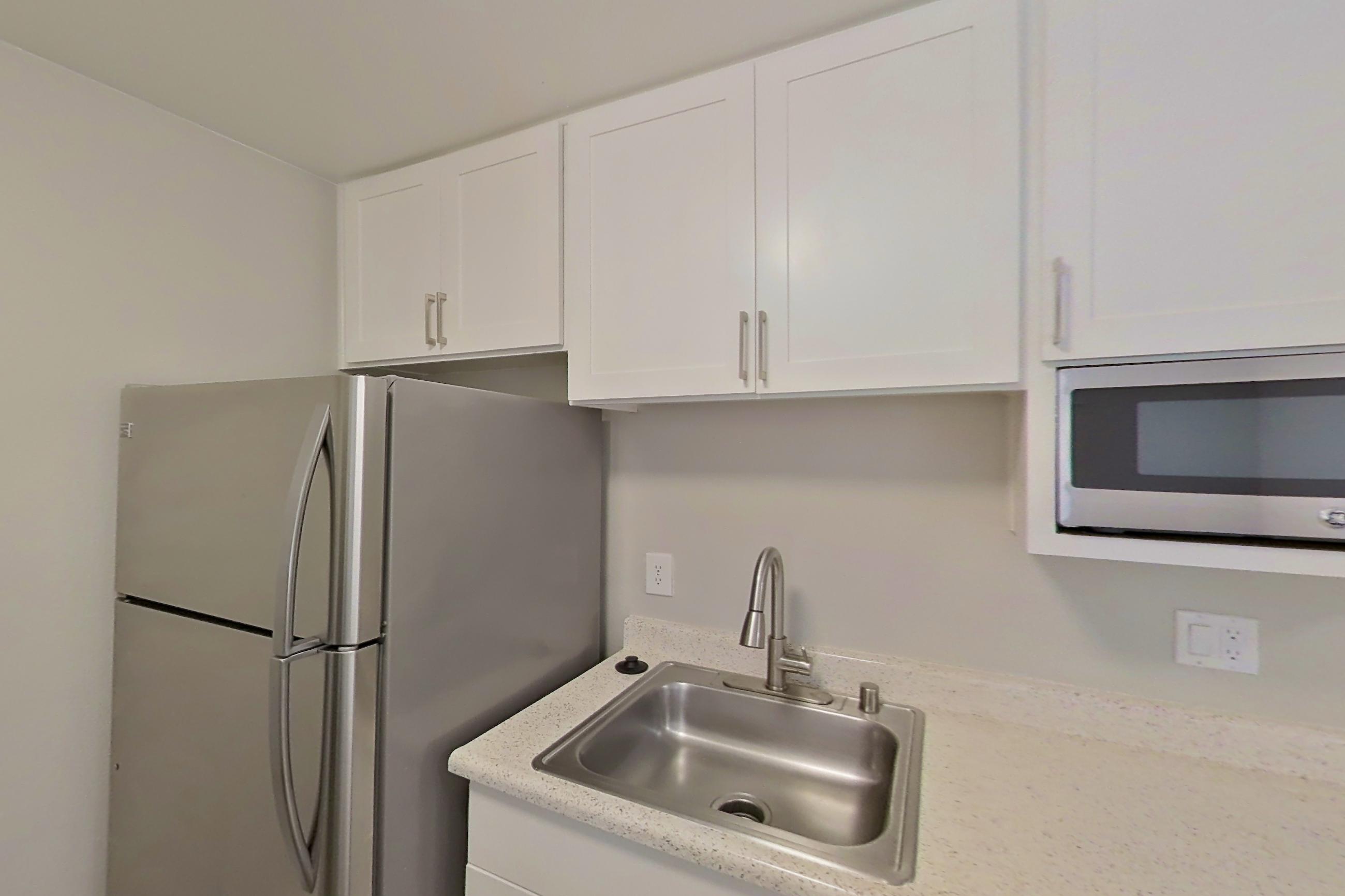 Kitchen with dishwasher, electric range, light countertops, light stone countertops, light wood-finish flooring, microwave, oven/range, refrigerator, stainless steel appliances, and white appliances, Apartment 14-02 at Avana Rancho Cucamonga