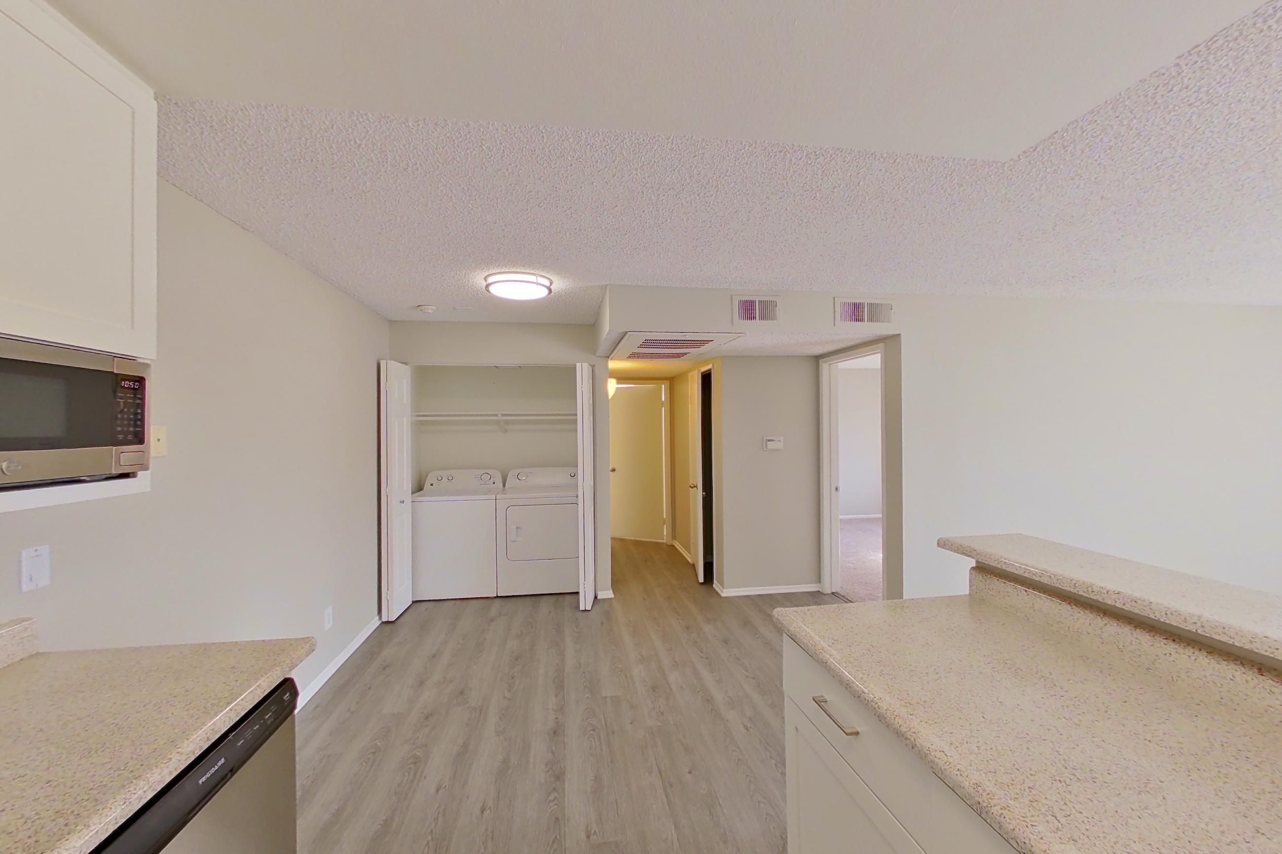 Kitchen with dishwasher, electric range, in-unit laundry, light countertops, light stone countertops, light wood-finish flooring, oven/range, range hood, refrigerator, and stainless steel appliances, Apartment 15-06 at Avana Rancho Cucamonga