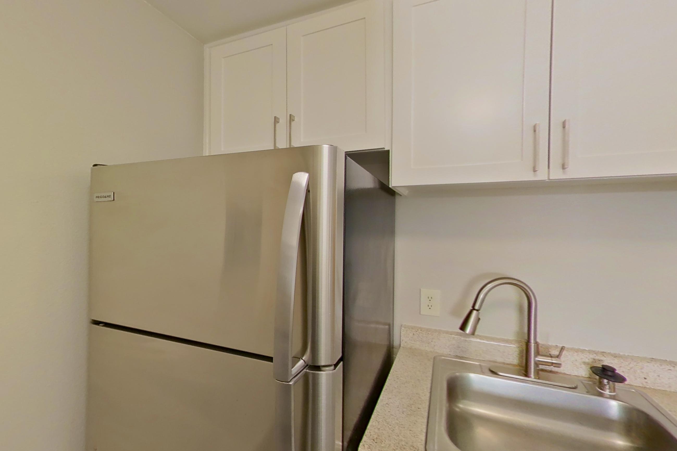 Kitchen with dishwasher, electric range, in-unit laundry, light countertops, light stone countertops, light wood-finish flooring, oven/range, range hood, refrigerator, and stainless steel appliances, Apartment 15-06 at Avana Rancho Cucamonga