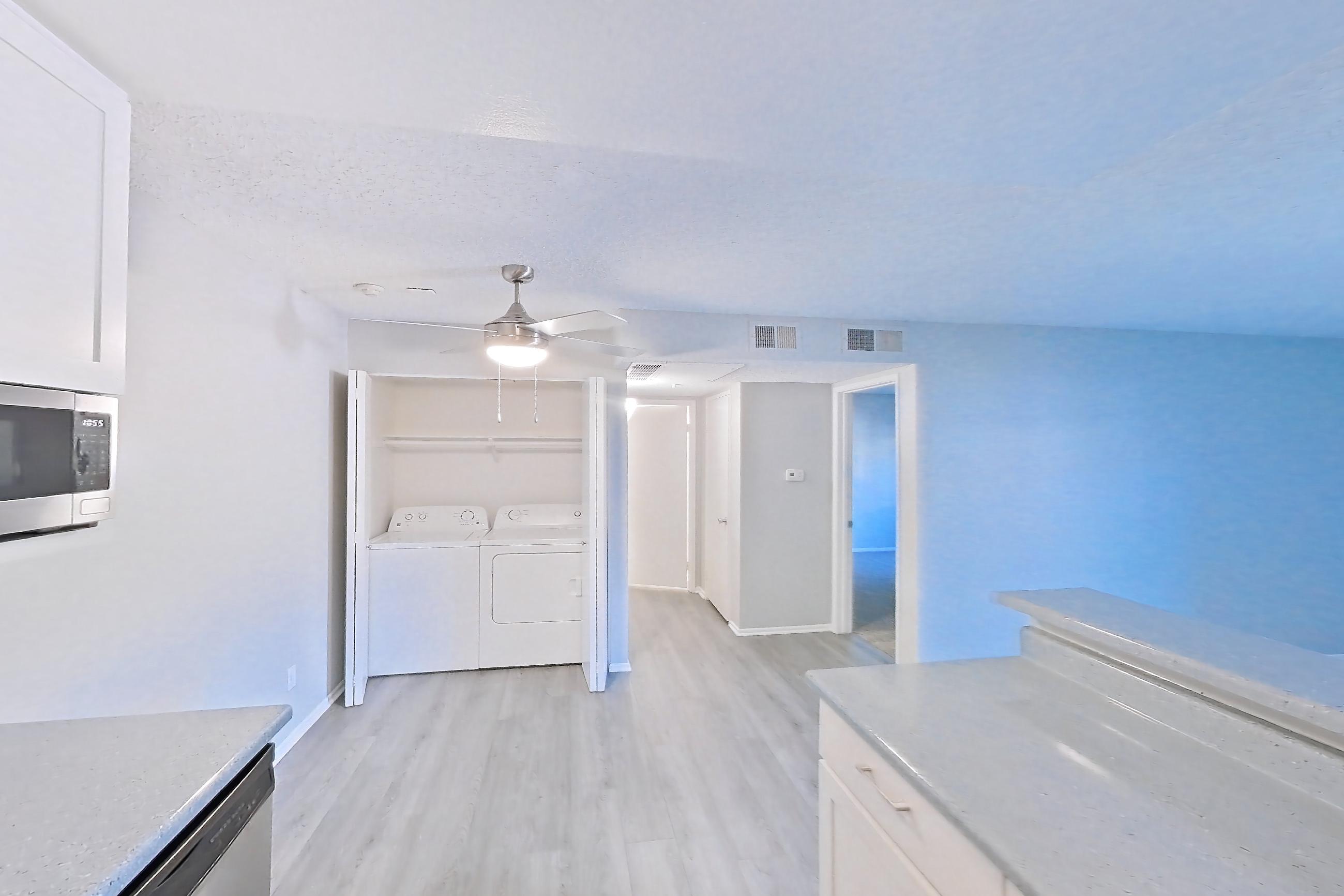 Kitchen with dishwasher, electric range, in-unit laundry, light countertops, light stone countertops, light wood-finish flooring, microwave, oven/range, refrigerator, and stainless steel appliances, Apartment 15-07 at Avana Rancho Cucamonga