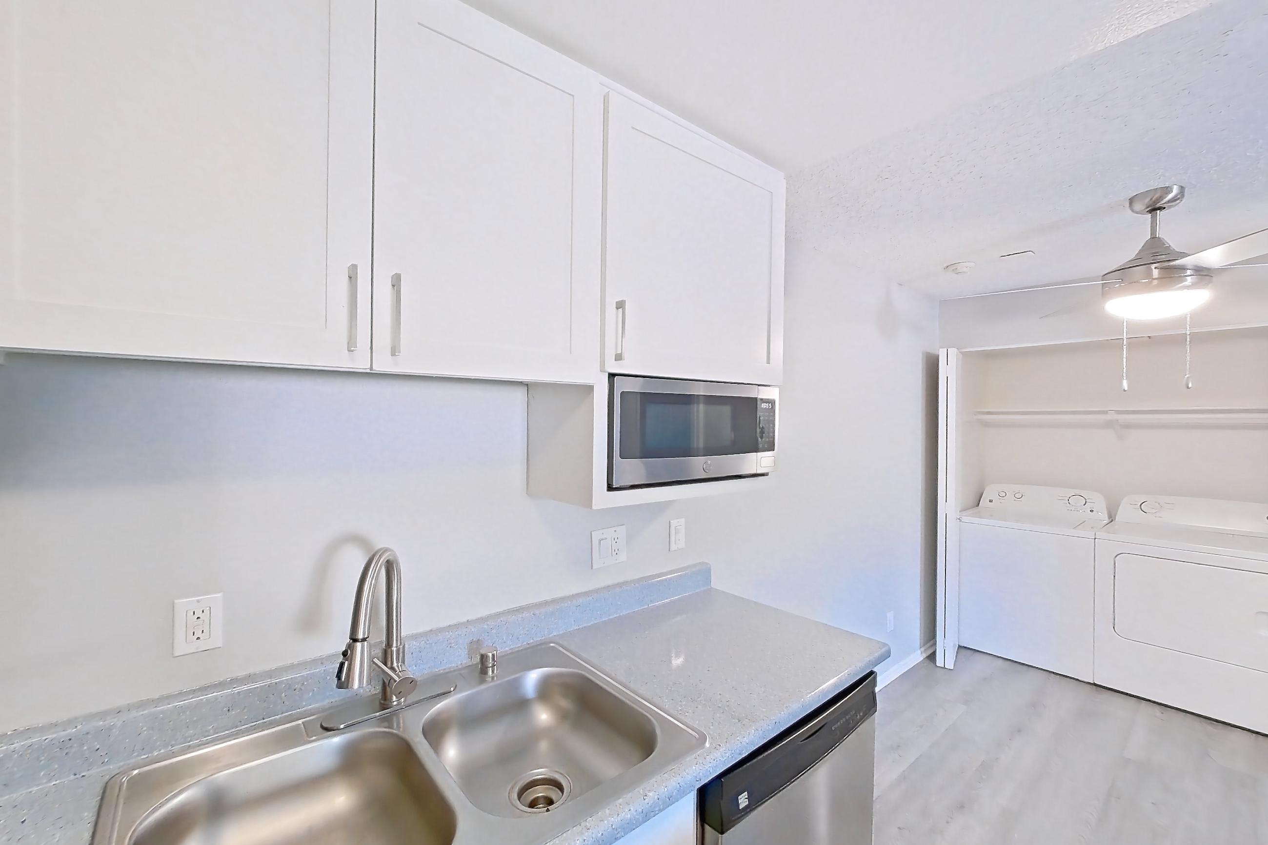 Kitchen with dishwasher, electric range, in-unit laundry, light countertops, light stone countertops, light wood-finish flooring, microwave, oven/range, refrigerator, and stainless steel appliances, Apartment 15-07 at Avana Rancho Cucamonga