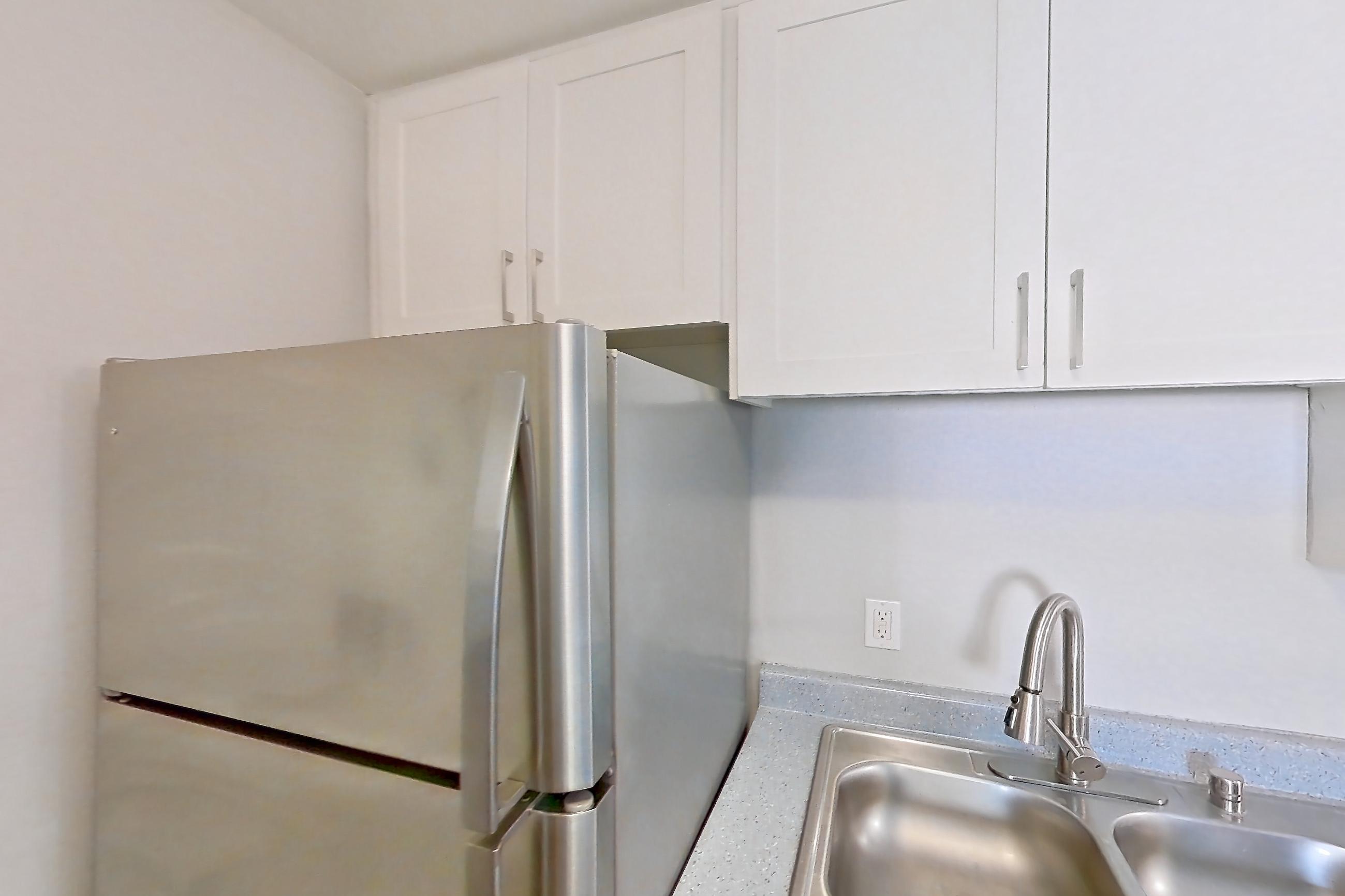 Kitchen with dishwasher, electric range, in-unit laundry, light countertops, light stone countertops, light wood-finish flooring, microwave, oven/range, refrigerator, and stainless steel appliances, Apartment 15-07 at Avana Rancho Cucamonga
