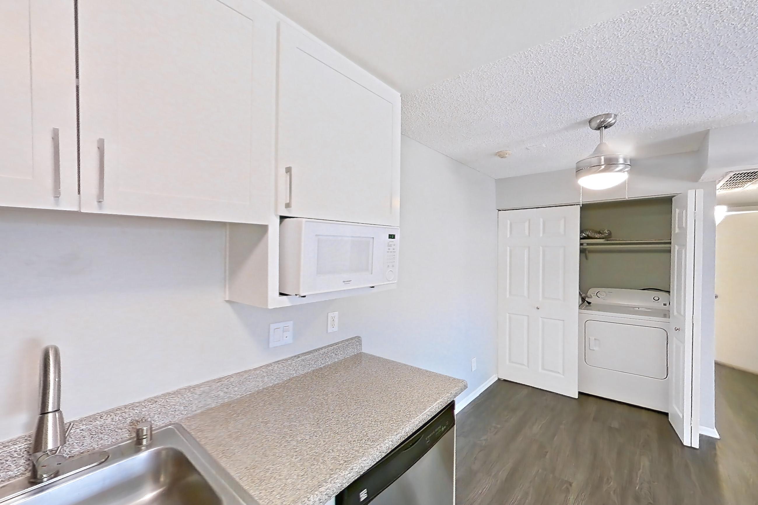Kitchen with dark wood-finish flooring, dishwasher, electric range, in-unit laundry, light countertops, light stone countertops, oven/range, and stainless steel appliances, Apartment 15-18 at Avana Rancho Cucamonga