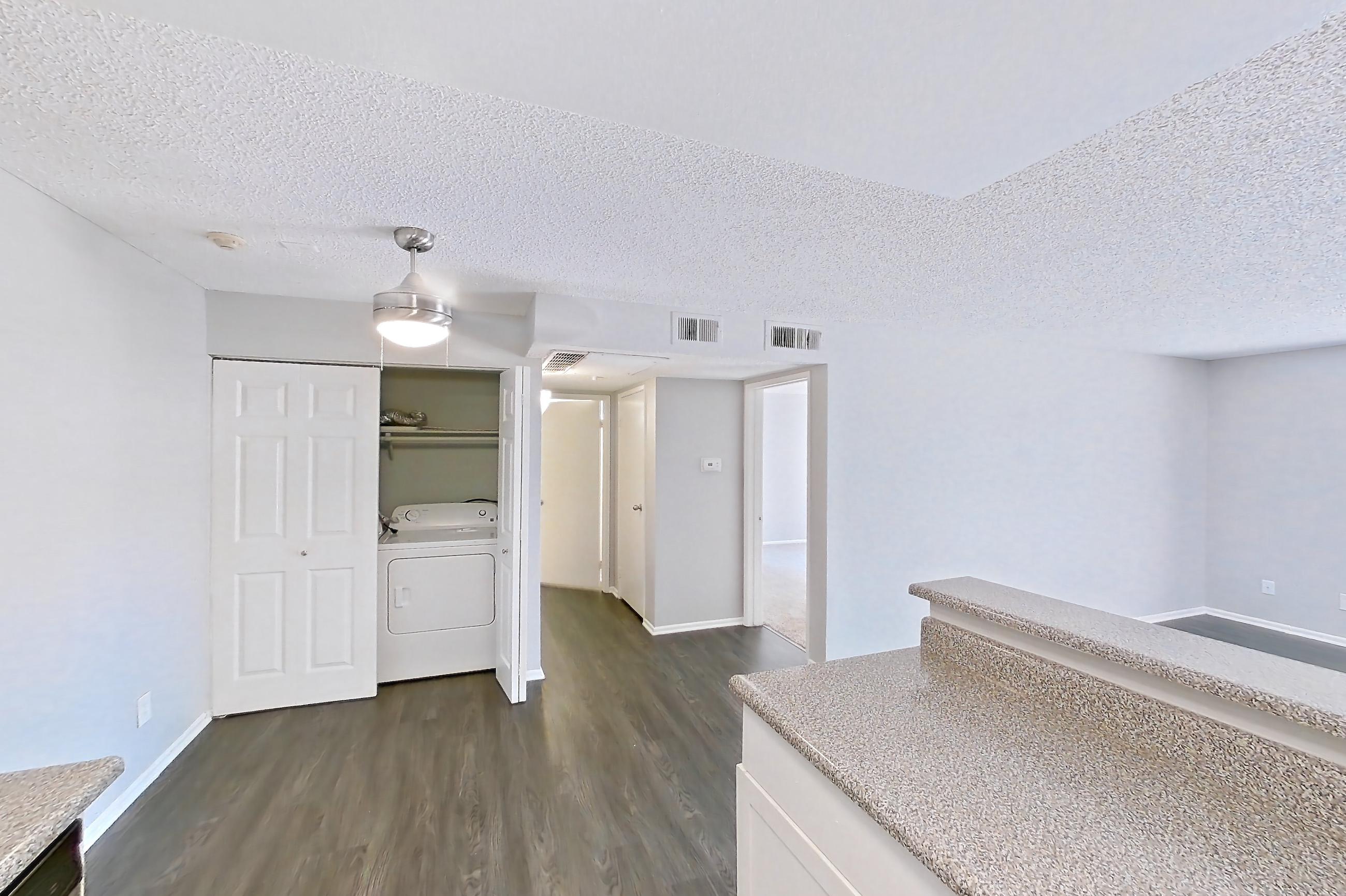 Kitchen with dark wood-finish flooring, dishwasher, electric range, in-unit laundry, light countertops, light stone countertops, oven/range, and stainless steel appliances, Apartment 15-18 at Avana Rancho Cucamonga