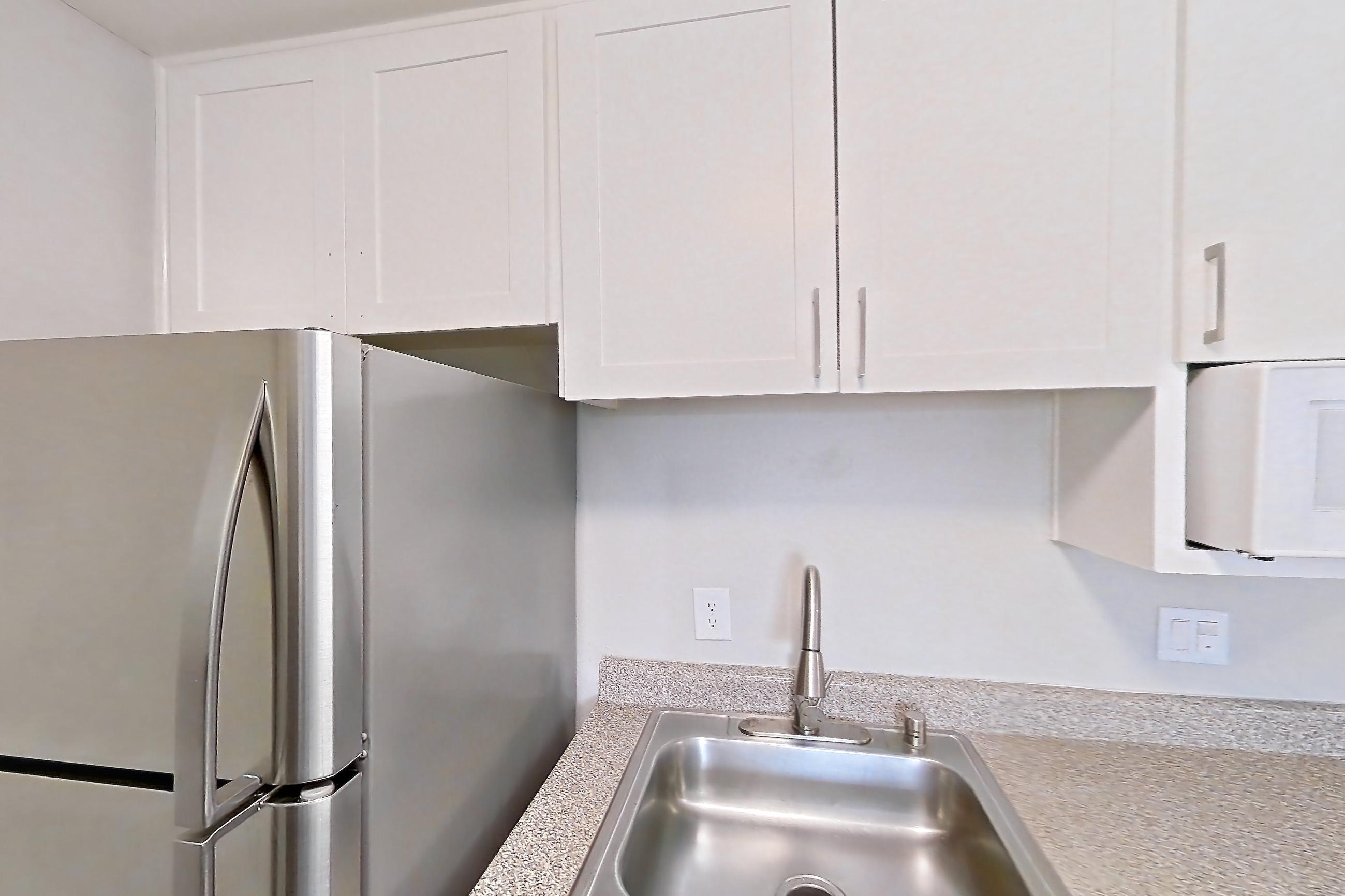 Kitchen with dark wood-finish flooring, dishwasher, electric range, in-unit laundry, light countertops, light stone countertops, oven/range, and stainless steel appliances, Apartment 15-18 at Avana Rancho Cucamonga