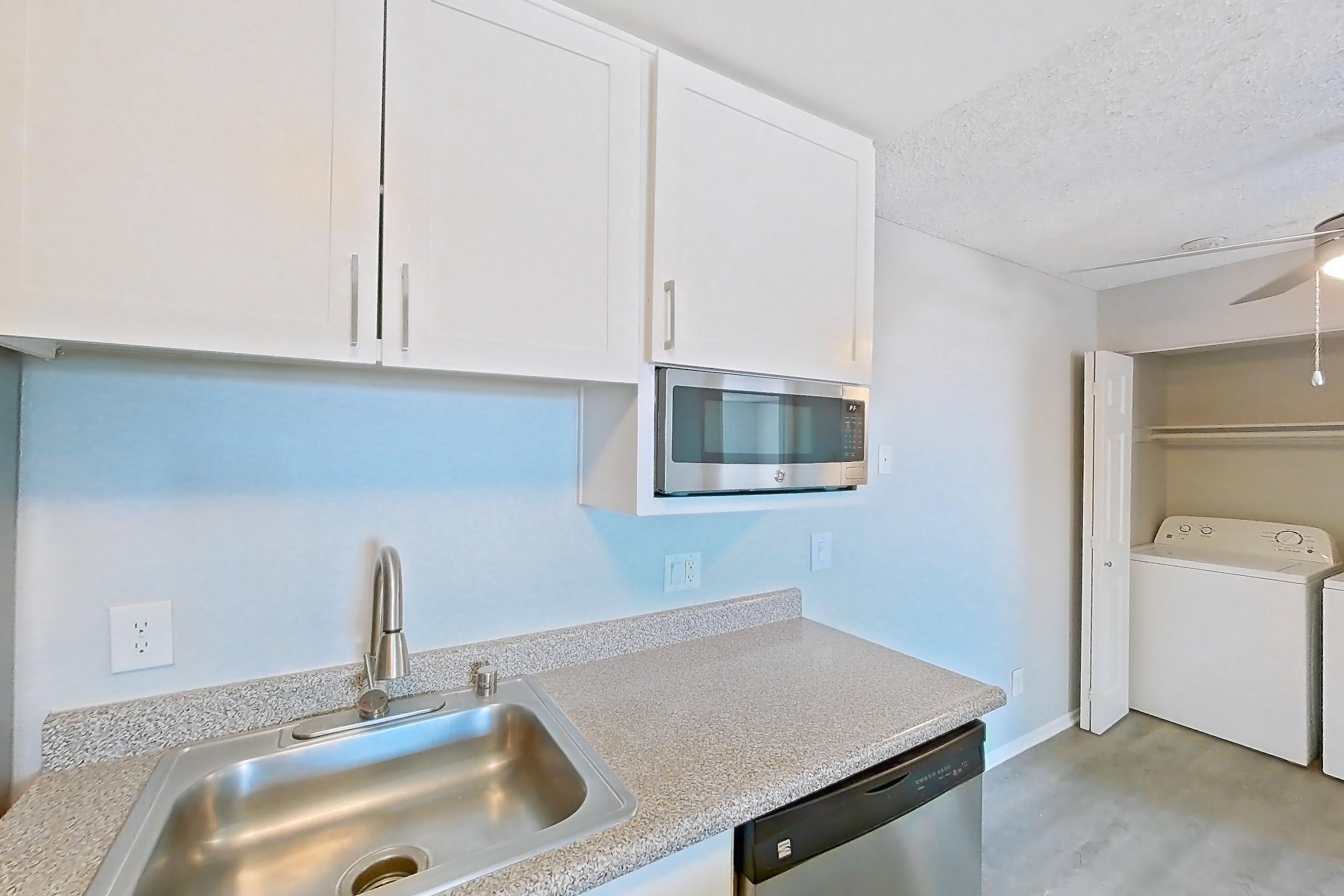 Kitchen with black appliances, dishwasher, electric range, in-unit laundry, light countertops, light stone countertops, light wood-finish flooring, microwave, oven/range, and stainless steel appliances, Apartment 15-22 at Avana Rancho Cucamonga