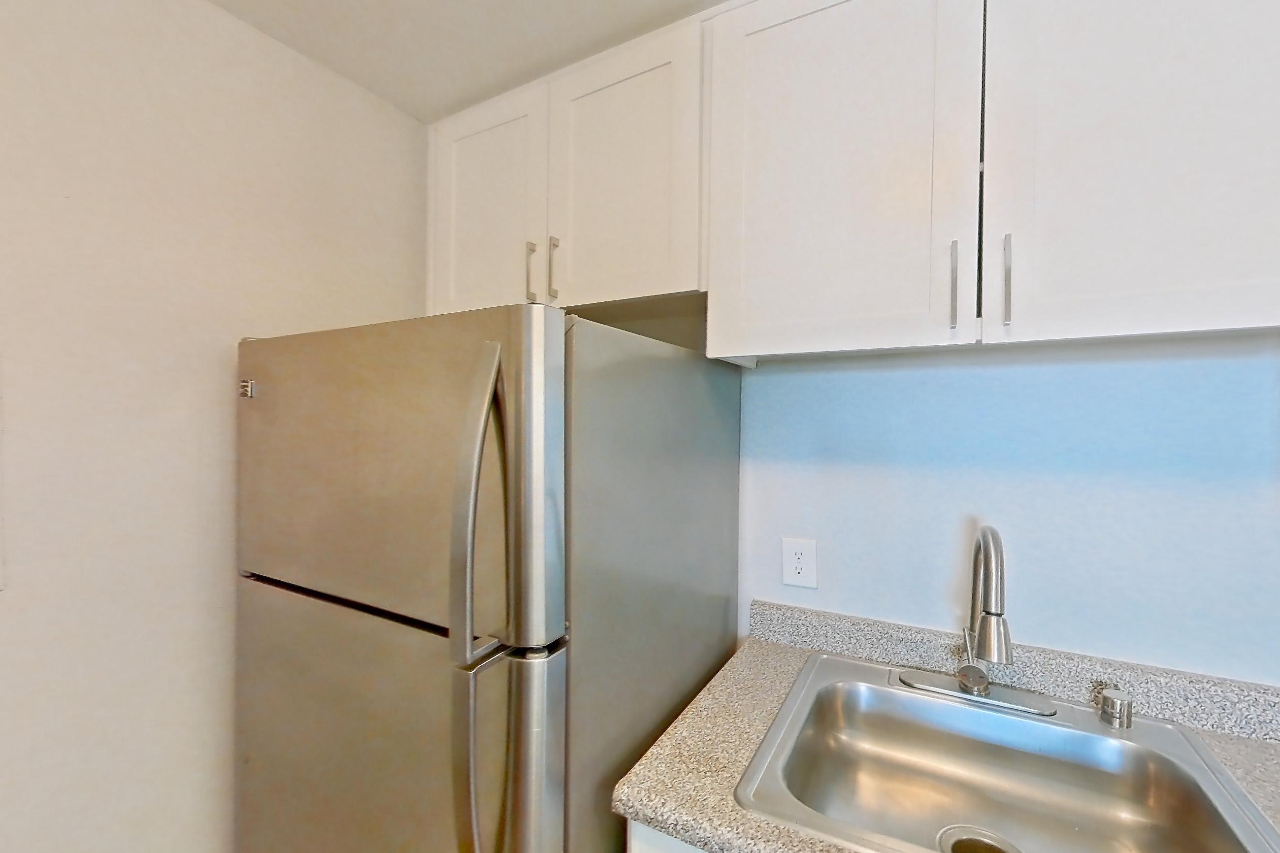 Kitchen with black appliances, dishwasher, electric range, in-unit laundry, light countertops, light stone countertops, light wood-finish flooring, microwave, oven/range, and stainless steel appliances, Apartment 15-22 at Avana Rancho Cucamonga