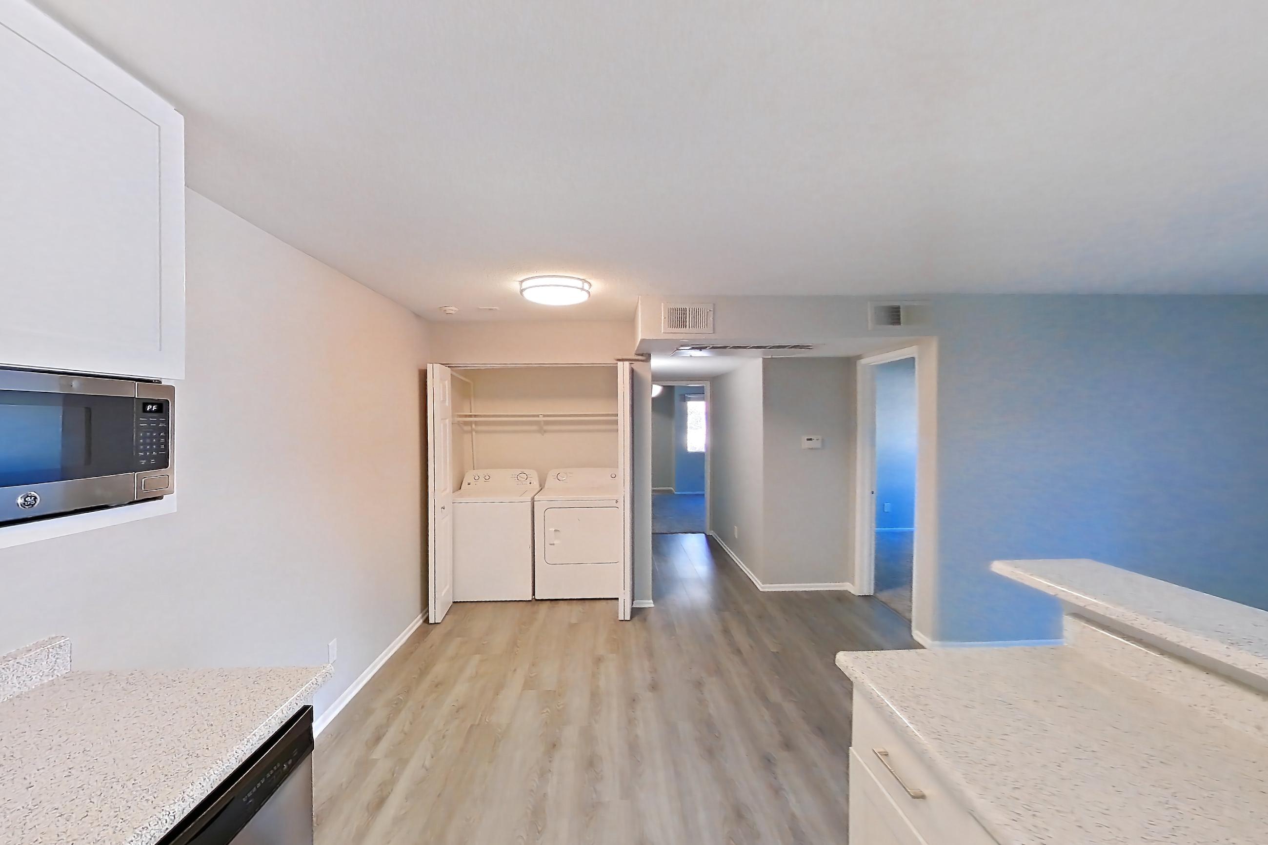 Kitchen with black appliances, electric range, in-unit laundry, light stone countertops, light wood-finish flooring, oven/range, refrigerator, and stainless steel appliances, Apartment 16-06 at Avana Rancho Cucamonga