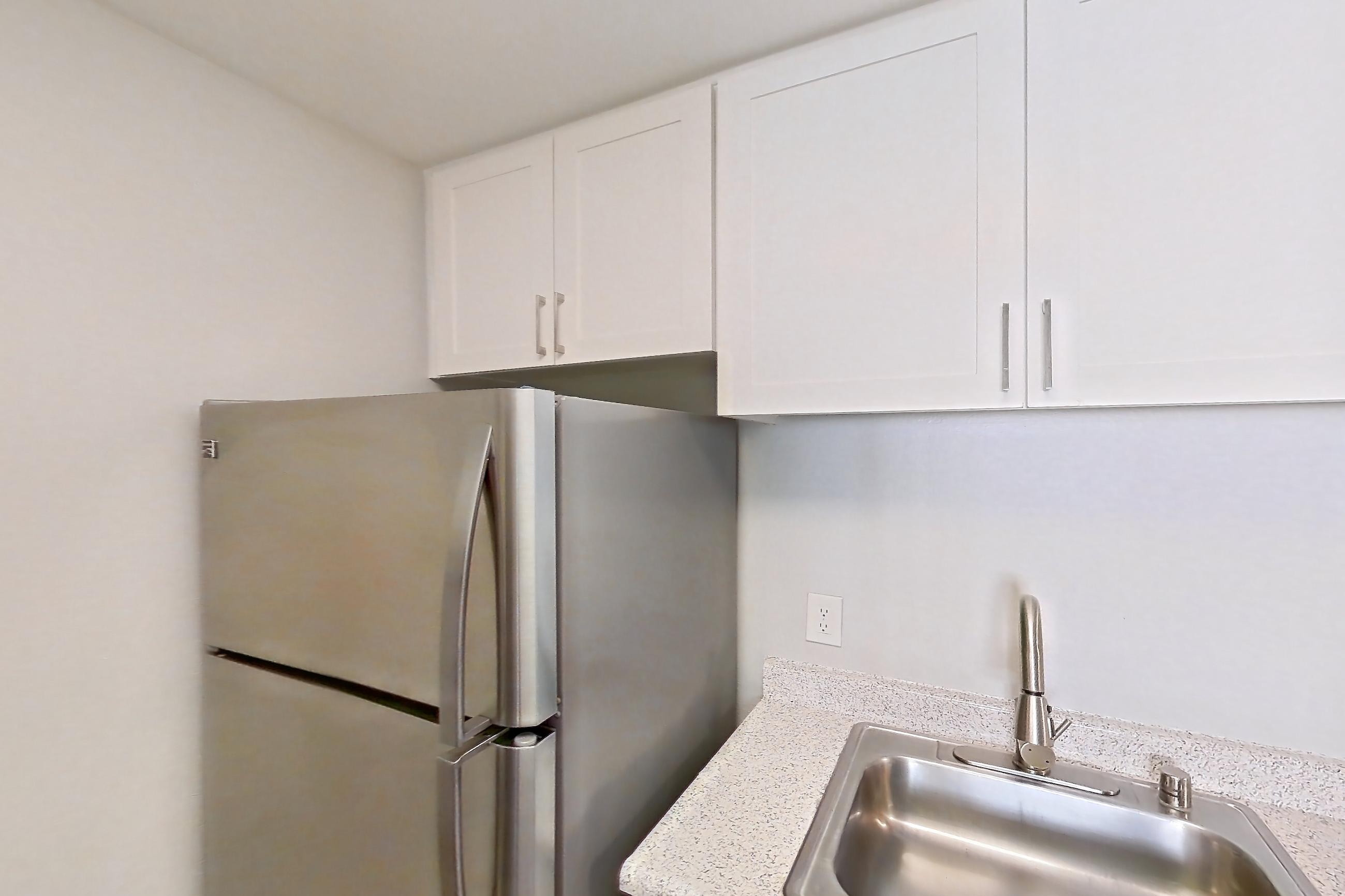 Kitchen with black appliances, electric range, in-unit laundry, light stone countertops, light wood-finish flooring, oven/range, refrigerator, and stainless steel appliances, Apartment 16-06 at Avana Rancho Cucamonga