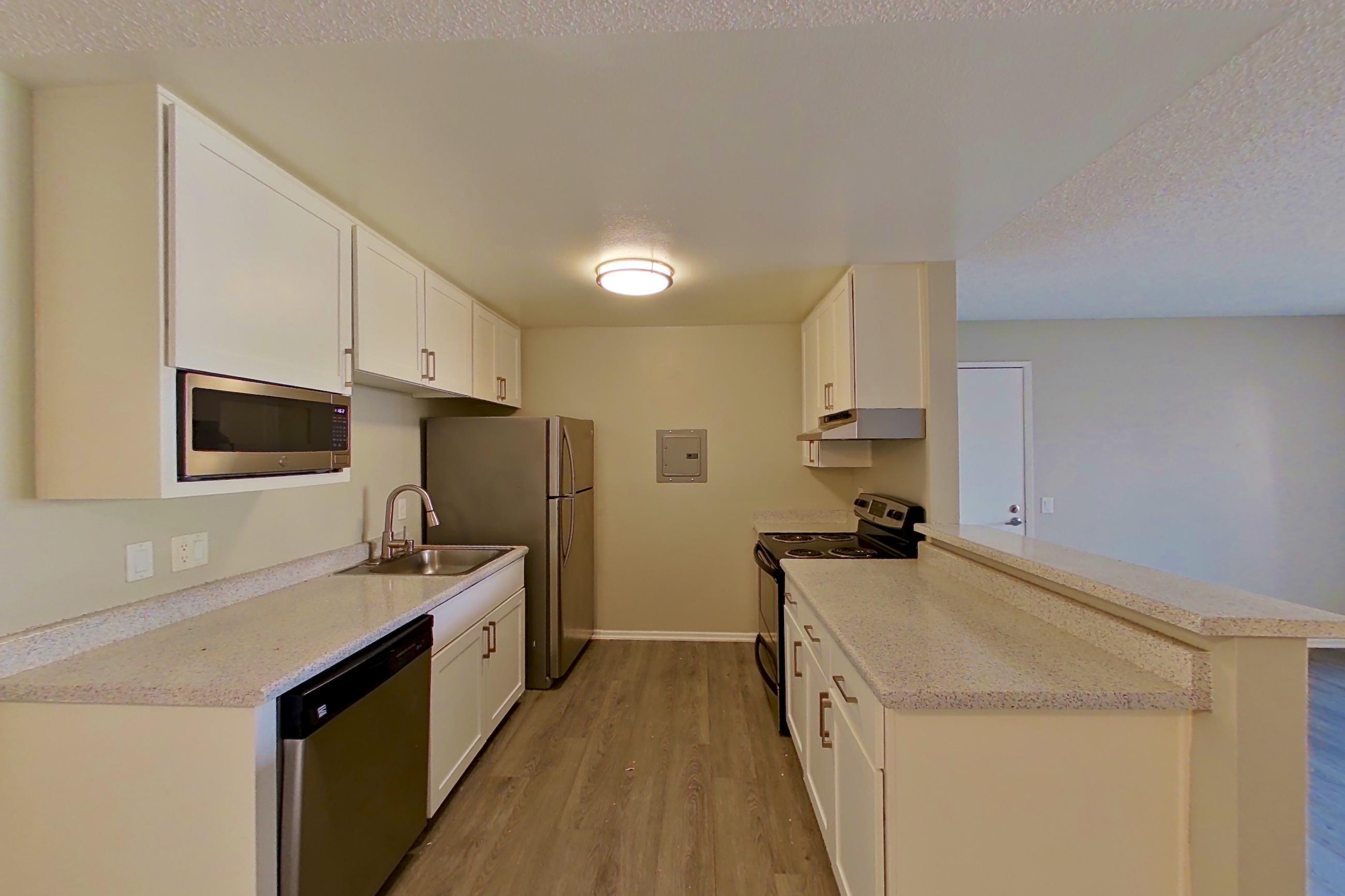 Dining area with dishwasher, electric range, in-unit laundry, light stone countertops, light wood-finish flooring, microwave, refrigerator, and stainless steel appliances, Apartment 16-08 at Avana Rancho Cucamonga