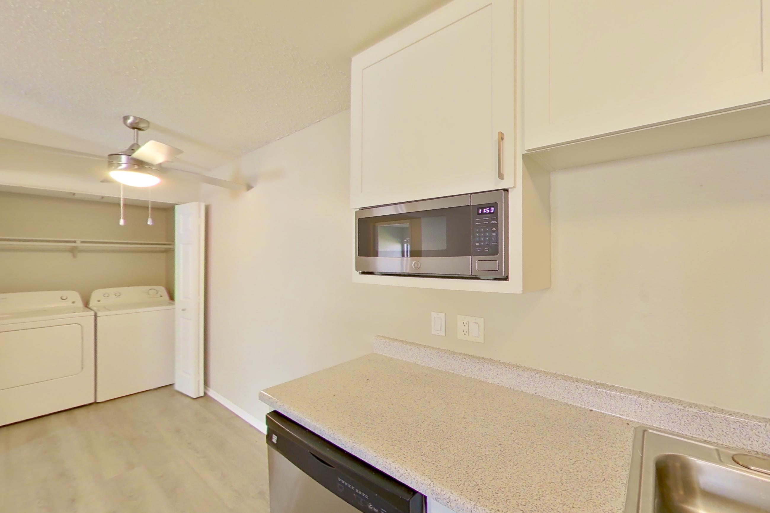Kitchen with dishwasher, electric range, in-unit laundry, light countertops, light stone countertops, light wood-finish flooring, microwave, oven/range, range hood, refrigerator, and stainless steel appliances, Apartment 16-08 at Avana Rancho Cucamonga