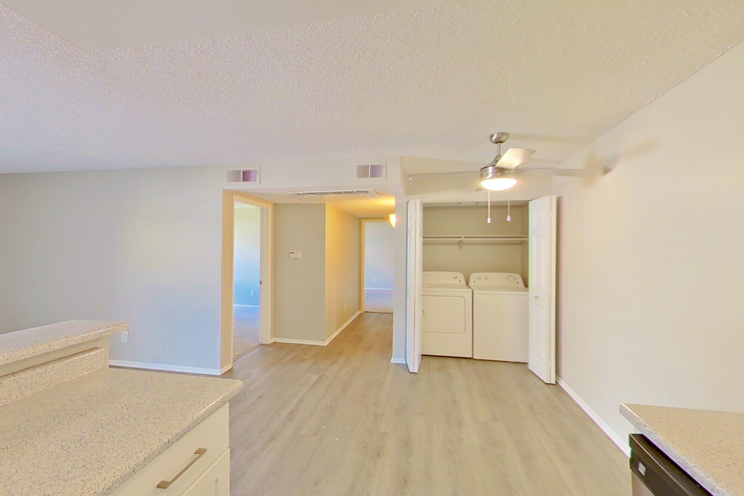 Kitchen with dishwasher, electric range, in-unit laundry, light countertops, light stone countertops, light wood-finish flooring, microwave, oven/range, range hood, refrigerator, and stainless steel appliances, Apartment 16-08 at Avana Rancho Cucamonga