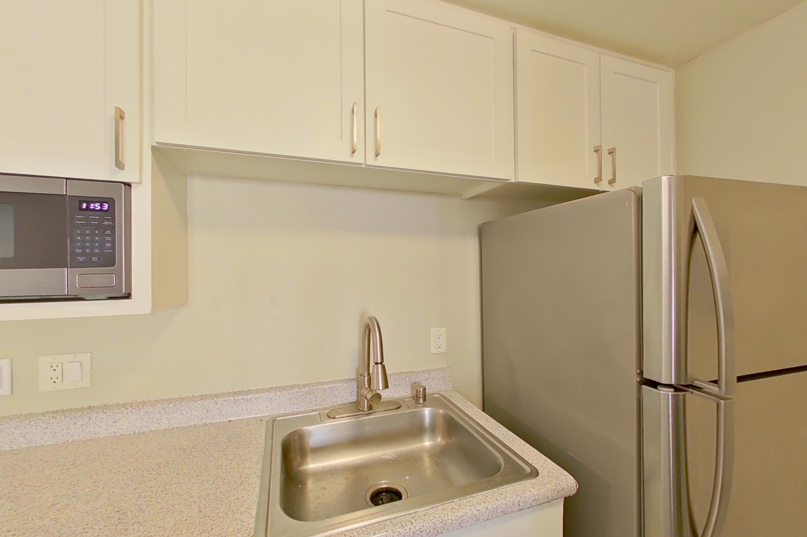 Kitchen with dishwasher, electric range, in-unit laundry, light countertops, light stone countertops, light wood-finish flooring, microwave, oven/range, range hood, refrigerator, and stainless steel appliances, Apartment 16-08 at Avana Rancho Cucamonga