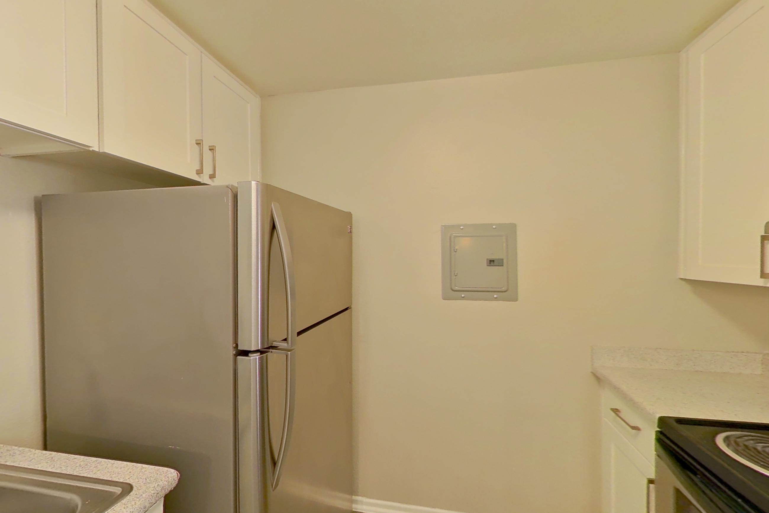 Kitchen with dishwasher, electric range, in-unit laundry, light countertops, light stone countertops, light wood-finish flooring, microwave, oven/range, range hood, refrigerator, and stainless steel appliances, Apartment 16-08 at Avana Rancho Cucamonga