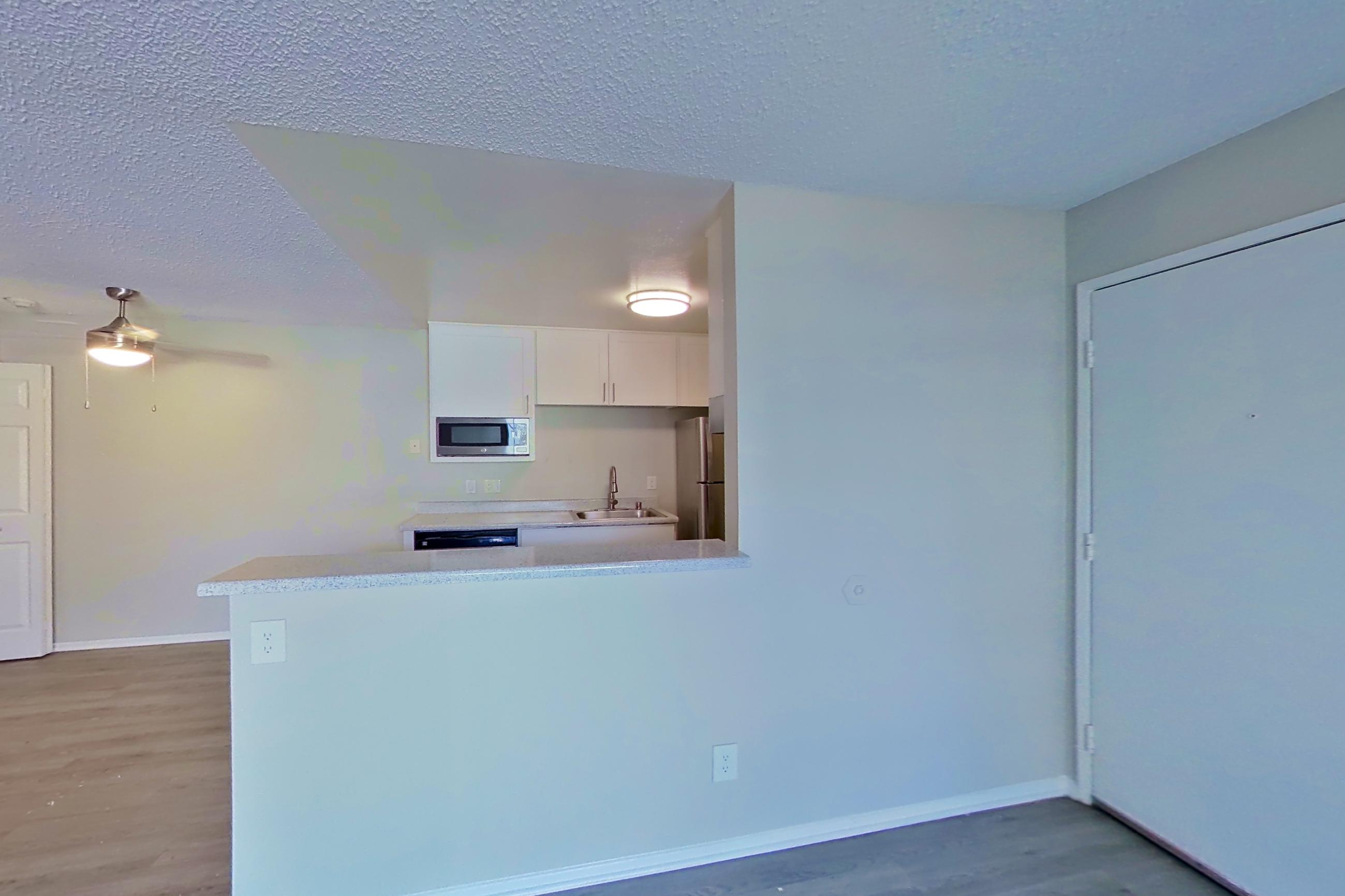 Living room with dark wood-finish flooring, in-unit laundry, refrigerator, and stainless steel appliances, Apartment 16-08 at Avana Rancho Cucamonga