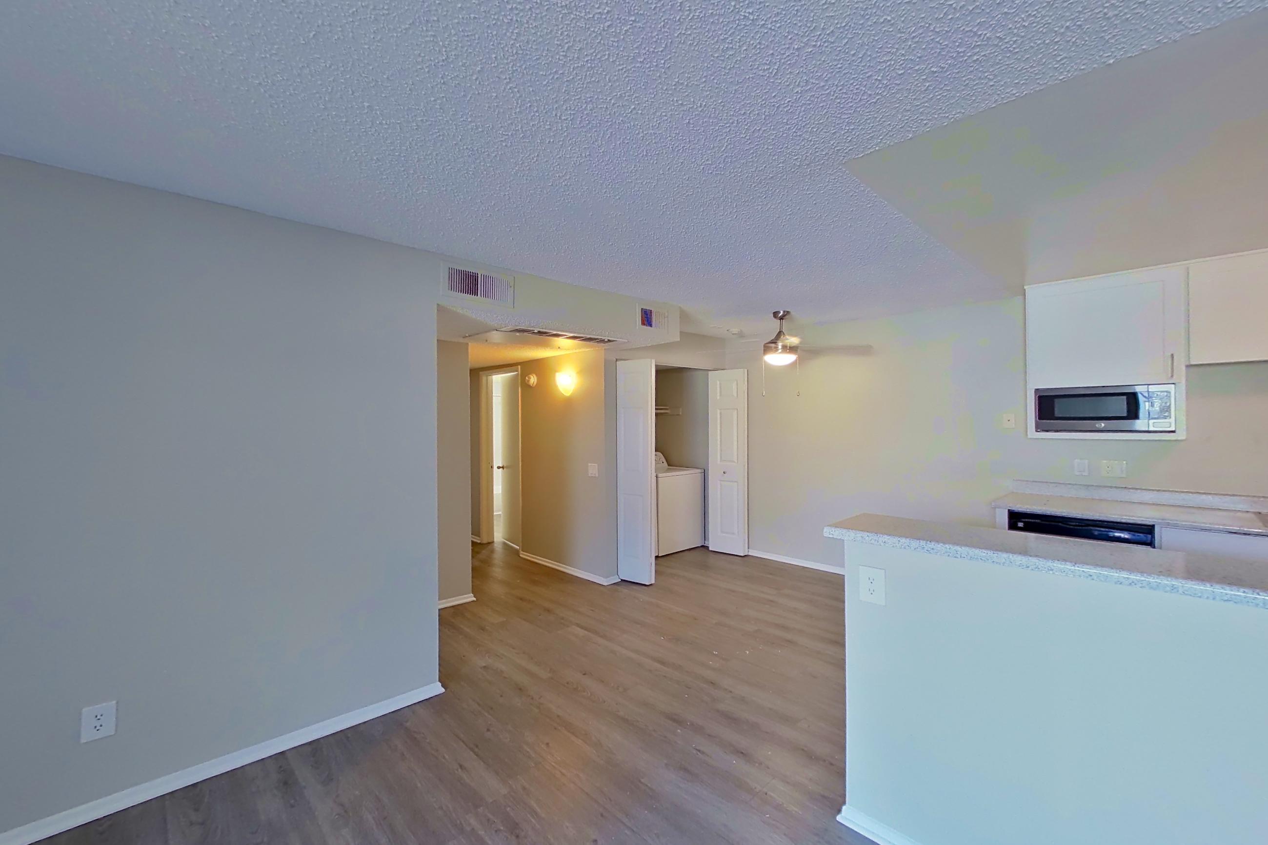 Living room with dark wood-finish flooring, in-unit laundry, refrigerator, and stainless steel appliances, Apartment 16-08 at Avana Rancho Cucamonga