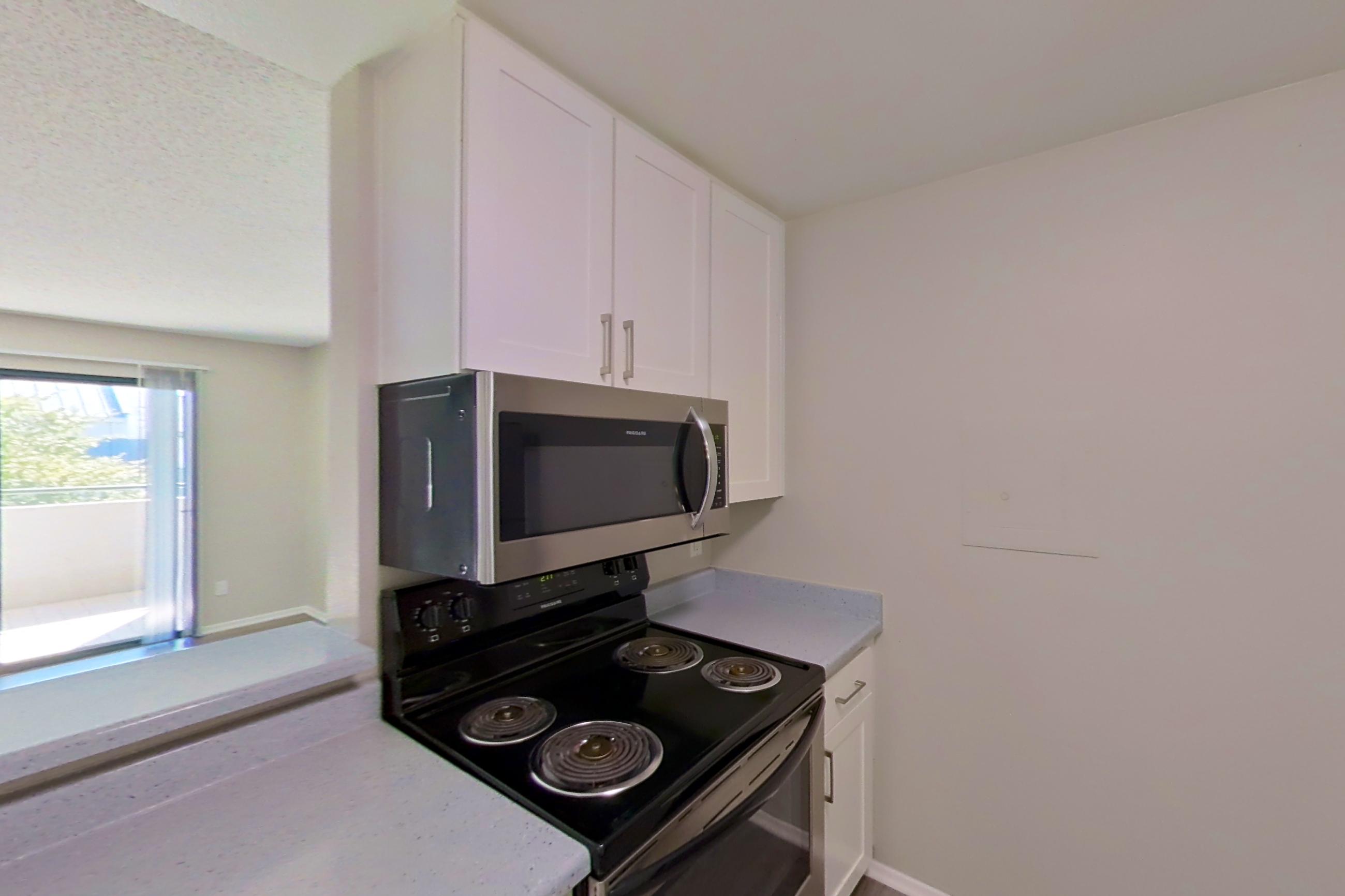 Kitchen with dishwasher, electric range, light countertops, light stone countertops, light wood-finish flooring, microwave, oven/range, refrigerator, and stainless steel appliances, Apartment 16-23 at Avana Rancho Cucamonga