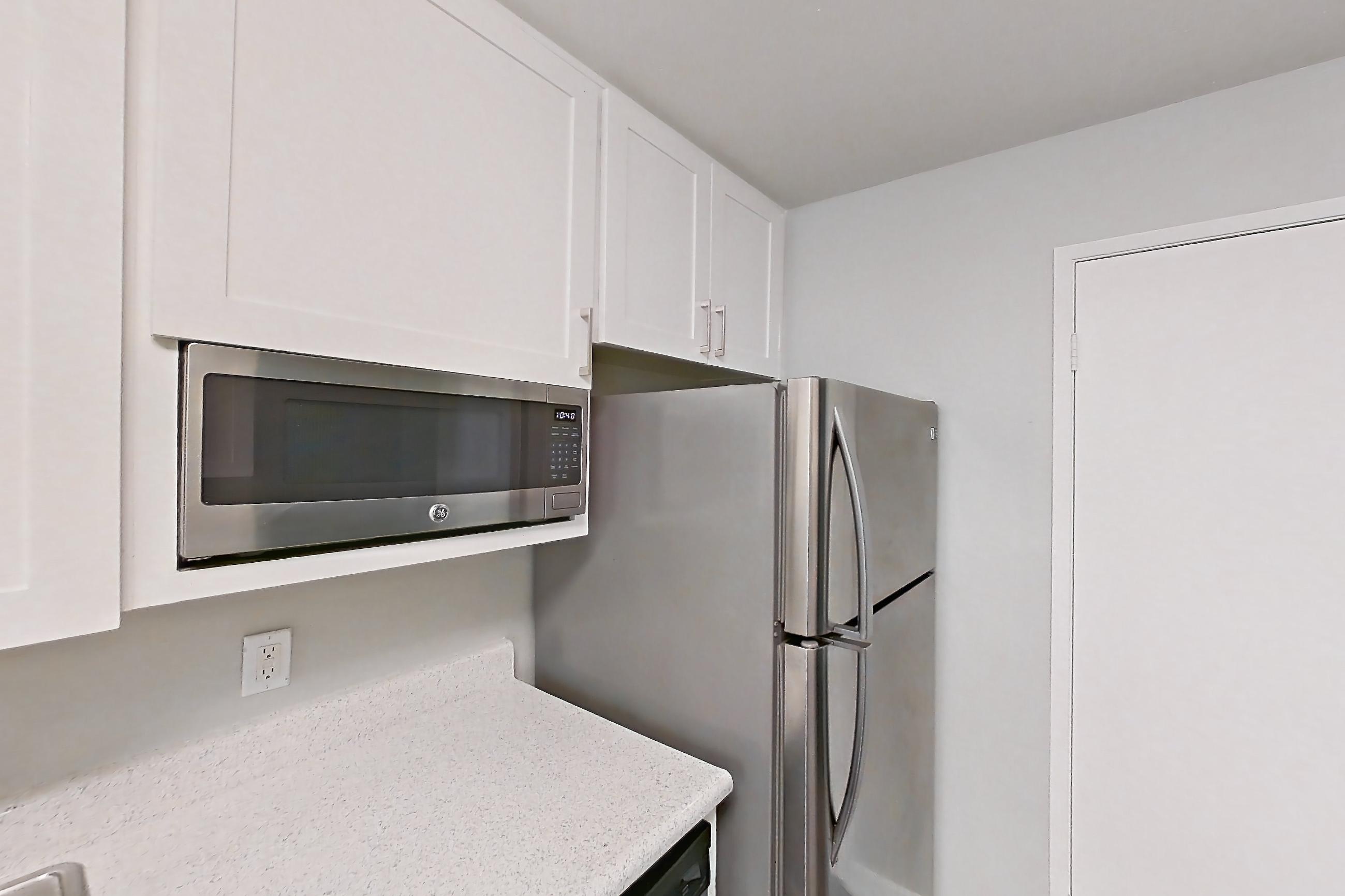 Kitchen with dark wood-finish flooring, dishwasher, electric range, light countertops, light stone countertops, light wood-finish flooring, microwave, oven/range, refrigerator, and stainless steel appliances, Apartment 17-01 at Avana Rancho Cucamonga