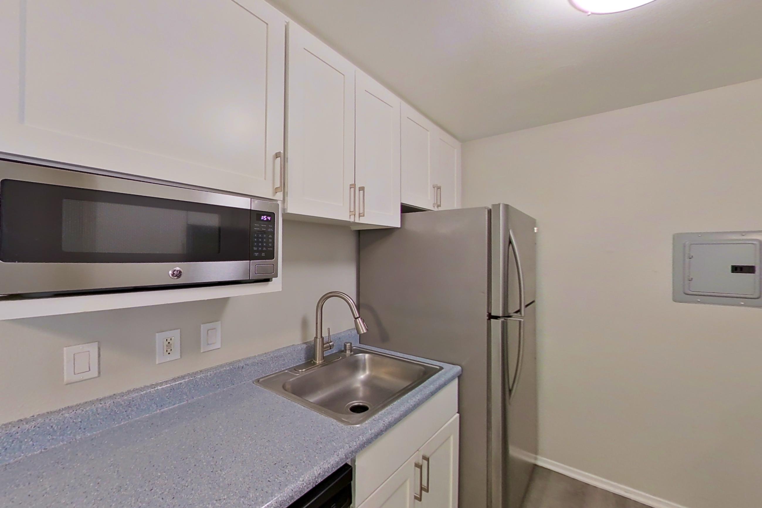 Kitchen with dishwasher, electric range, light stone countertops, light wood-finish flooring, microwave, oven/range, stainless steel appliances, and white appliances, Apartment 18-06 at Avana Rancho Cucamonga