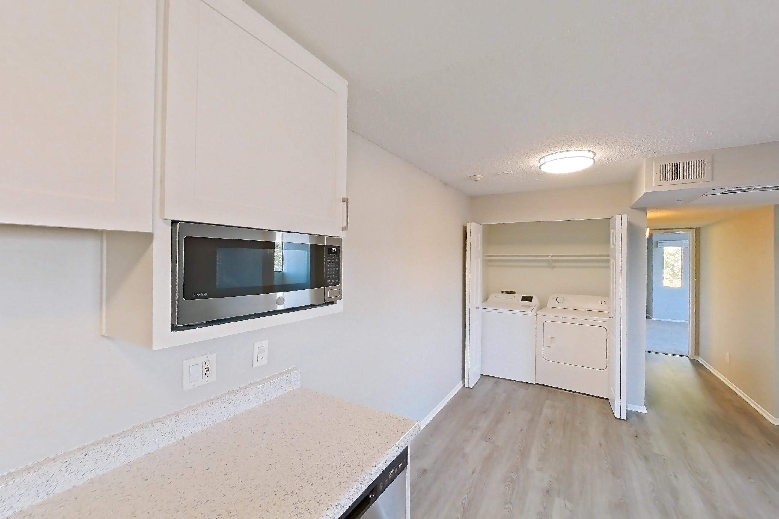 Kitchen with dishwasher, electric range, in-unit laundry, light countertops, light stone countertops, light wood-finish flooring, microwave, oven/range, refrigerator, and stainless steel appliances, Apartment 19-11 at Avana Rancho Cucamonga