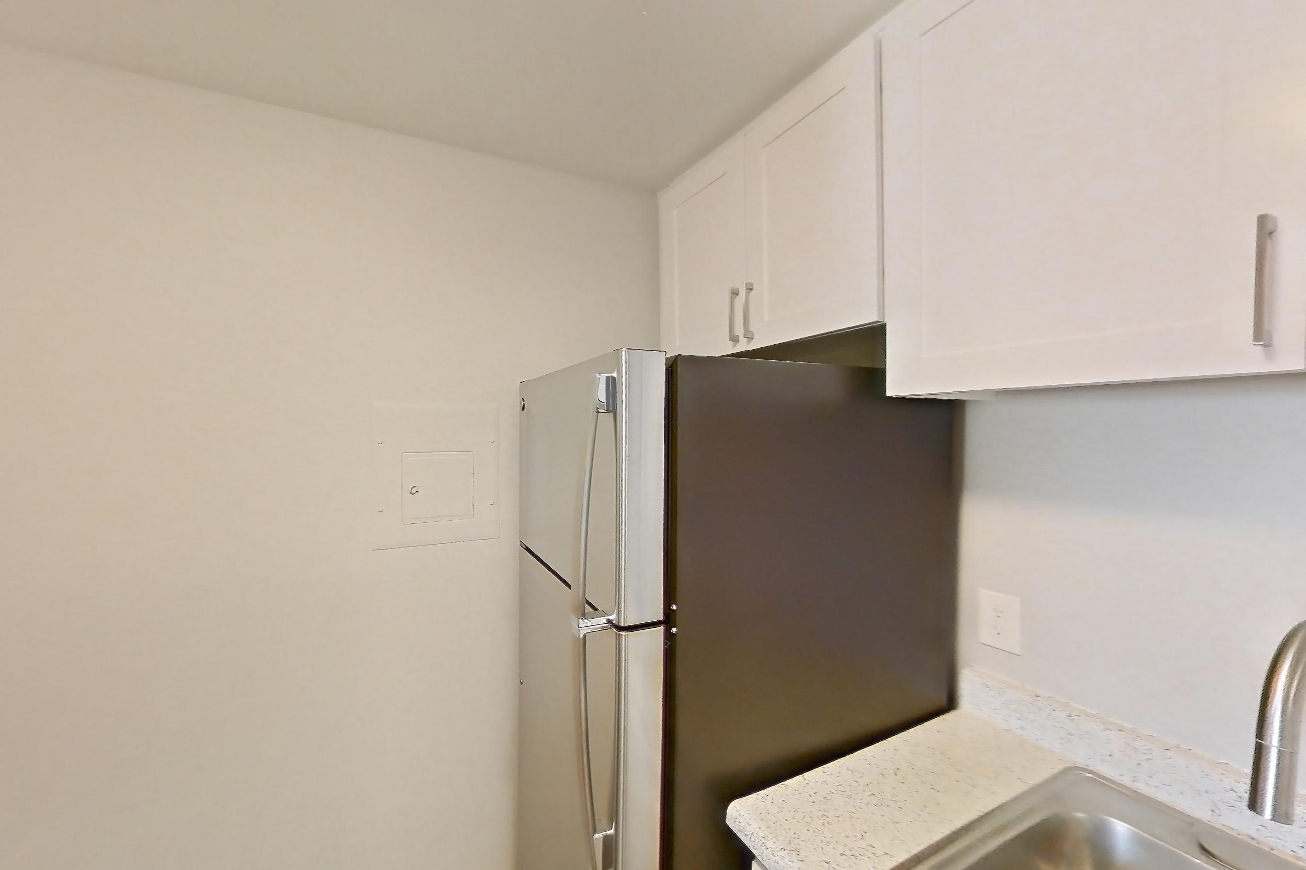 Kitchen with dishwasher, electric range, in-unit laundry, light countertops, light stone countertops, light wood-finish flooring, microwave, oven/range, refrigerator, and stainless steel appliances, Apartment 19-11 at Avana Rancho Cucamonga