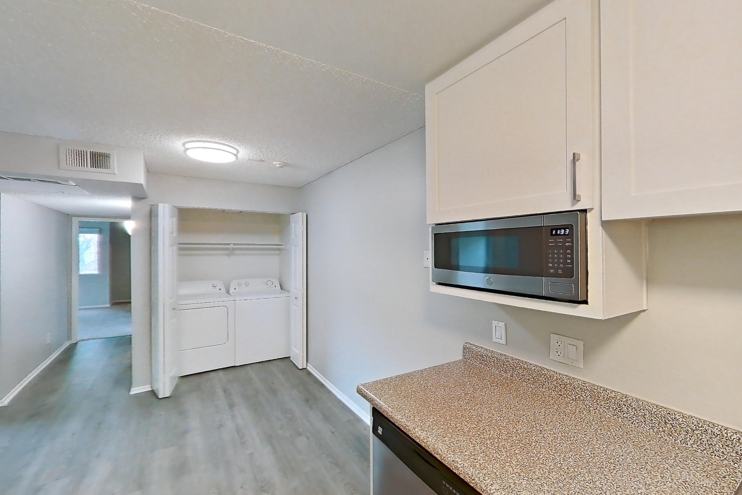 Kitchen with dishwasher, electric range, in-unit laundry, light stone countertops, light wood-finish flooring, oven/range, refrigerator, and stainless steel appliances, Apartment 20-05 at Avana Rancho Cucamonga