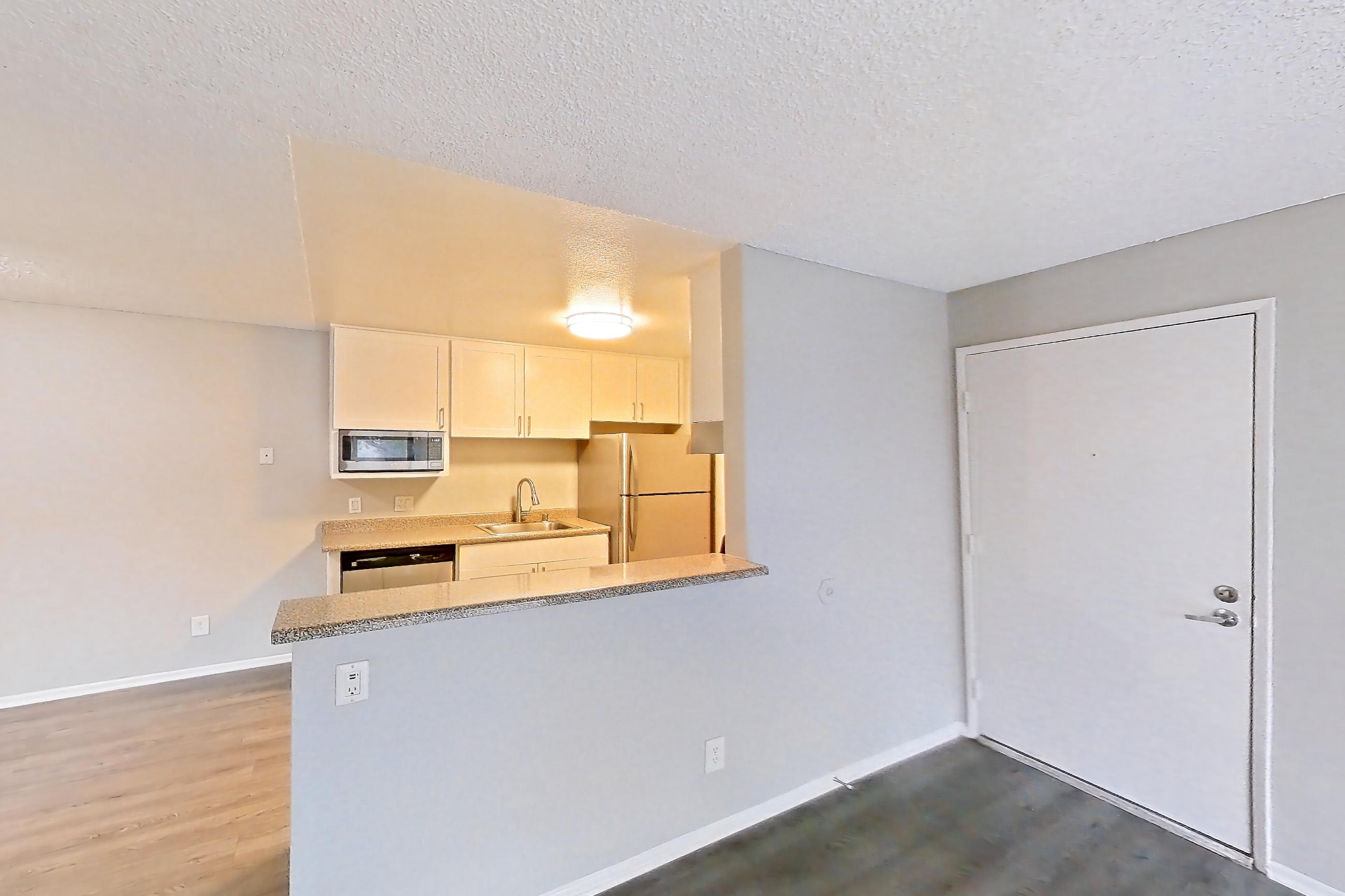 Living room with dark wood-finish flooring, light countertops, refrigerator, and white appliances, Apartment 20-05 at Avana Rancho Cucamonga