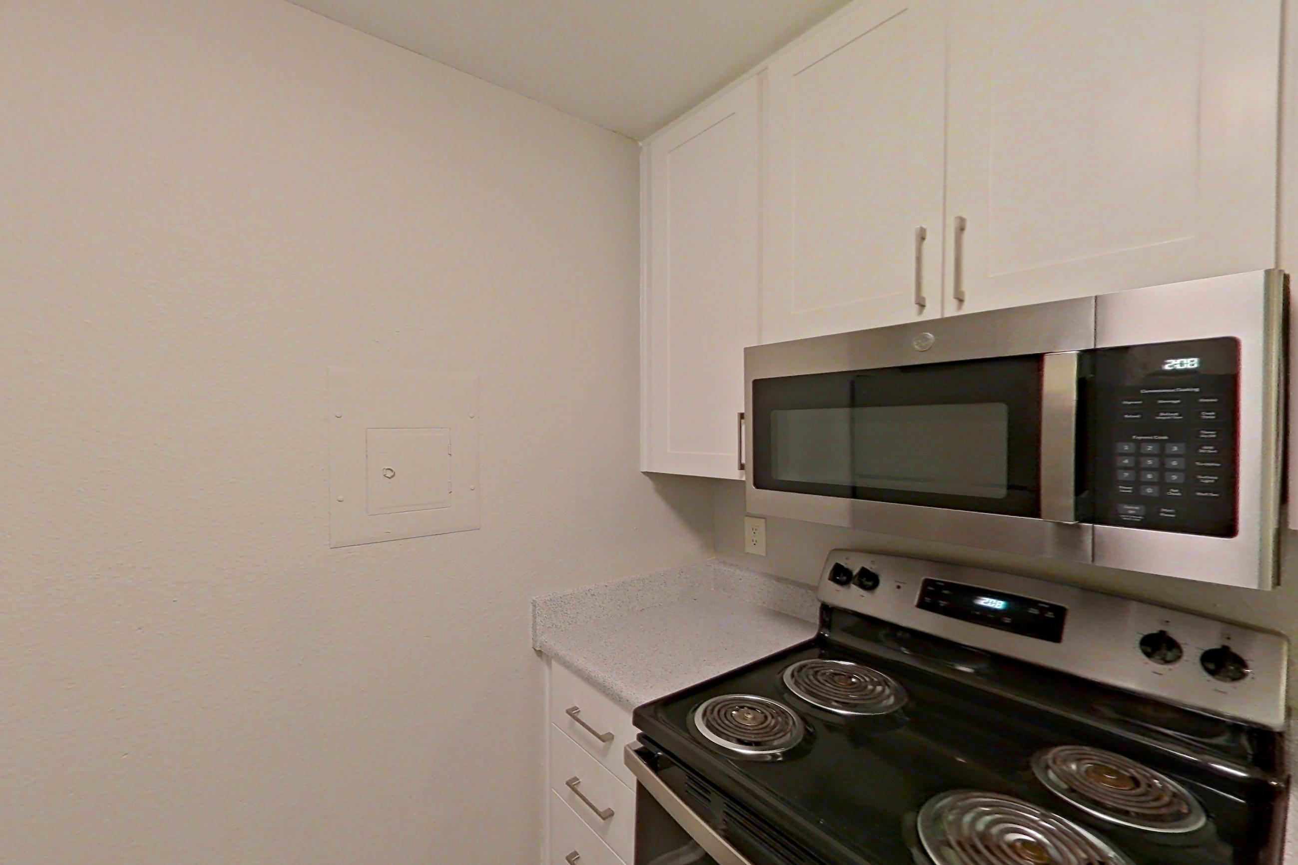 Kitchen with dishwasher, electric range, light countertops, light stone countertops, light wood-finish flooring, microwave, oven/range, refrigerator, and stainless steel appliances, Apartment 02-02 at Avana Rancho Cucamonga