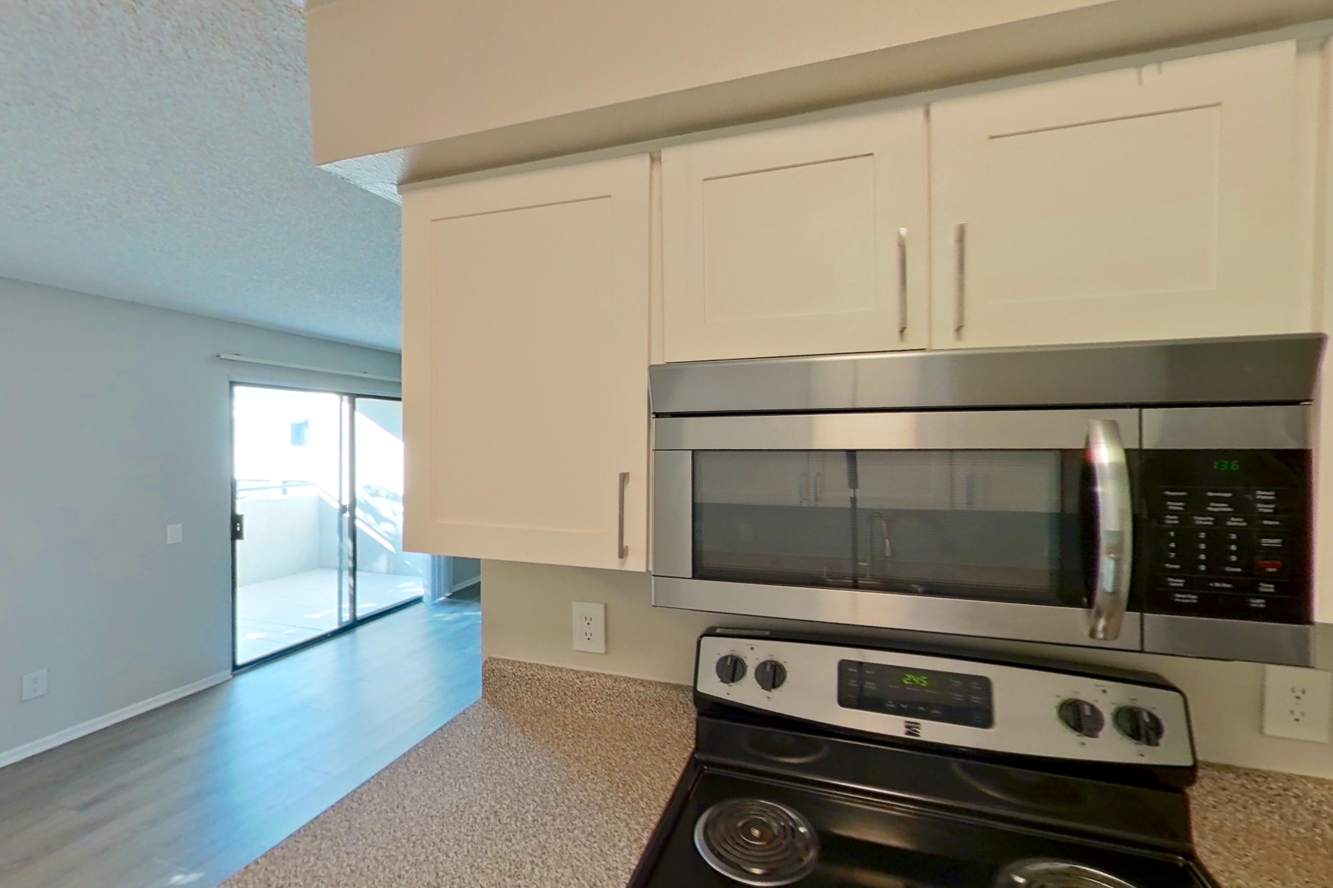 Kitchen with black appliances, dishwasher, electric range, light countertops, light stone countertops, light wood-finish flooring, microwave, oven/range, refrigerator, and stainless steel appliances, Apartment 07-03 at Avana Rancho Cucamonga