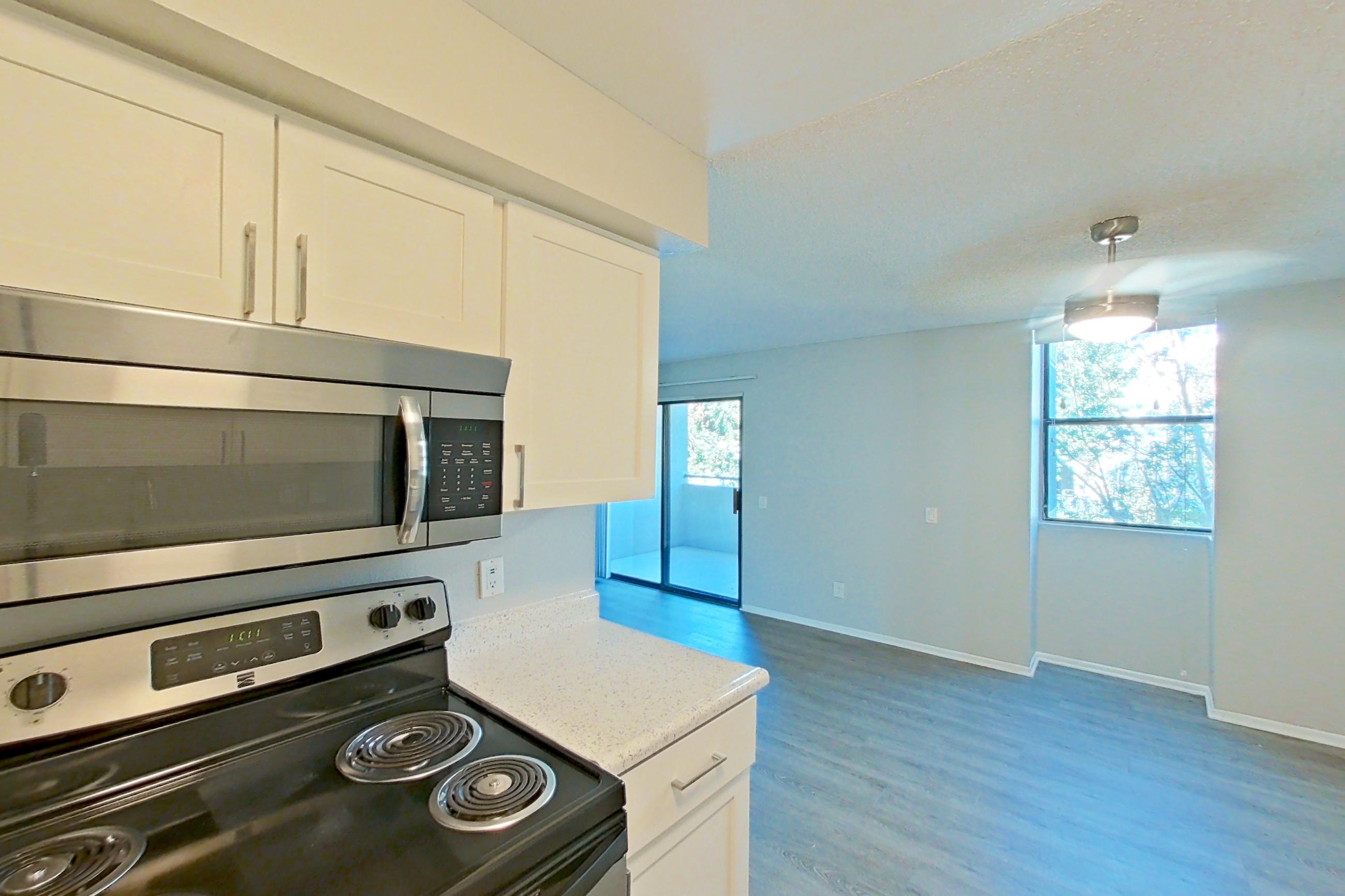 Kitchen with dishwasher, electric range, light stone countertops, light wood-finish flooring, microwave, oven/range, and stainless steel appliances, Apartment 09-05 at Avana Rancho Cucamonga