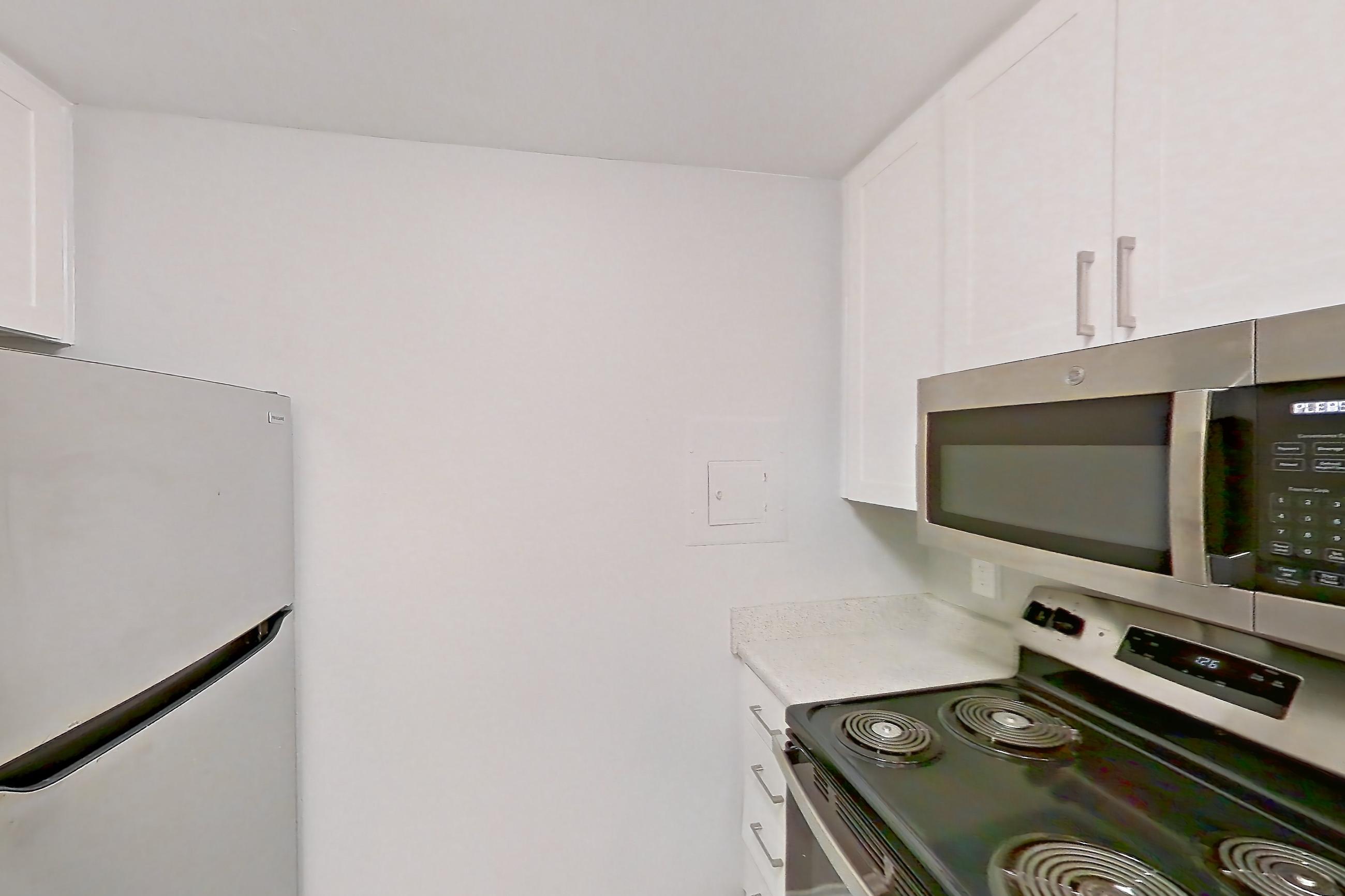 Kitchen with dishwasher, electric range, light countertops, light stone countertops, light wood-finish flooring, microwave, oven/range, and stainless steel appliances, Apartment 10-06 at Avana Rancho Cucamonga