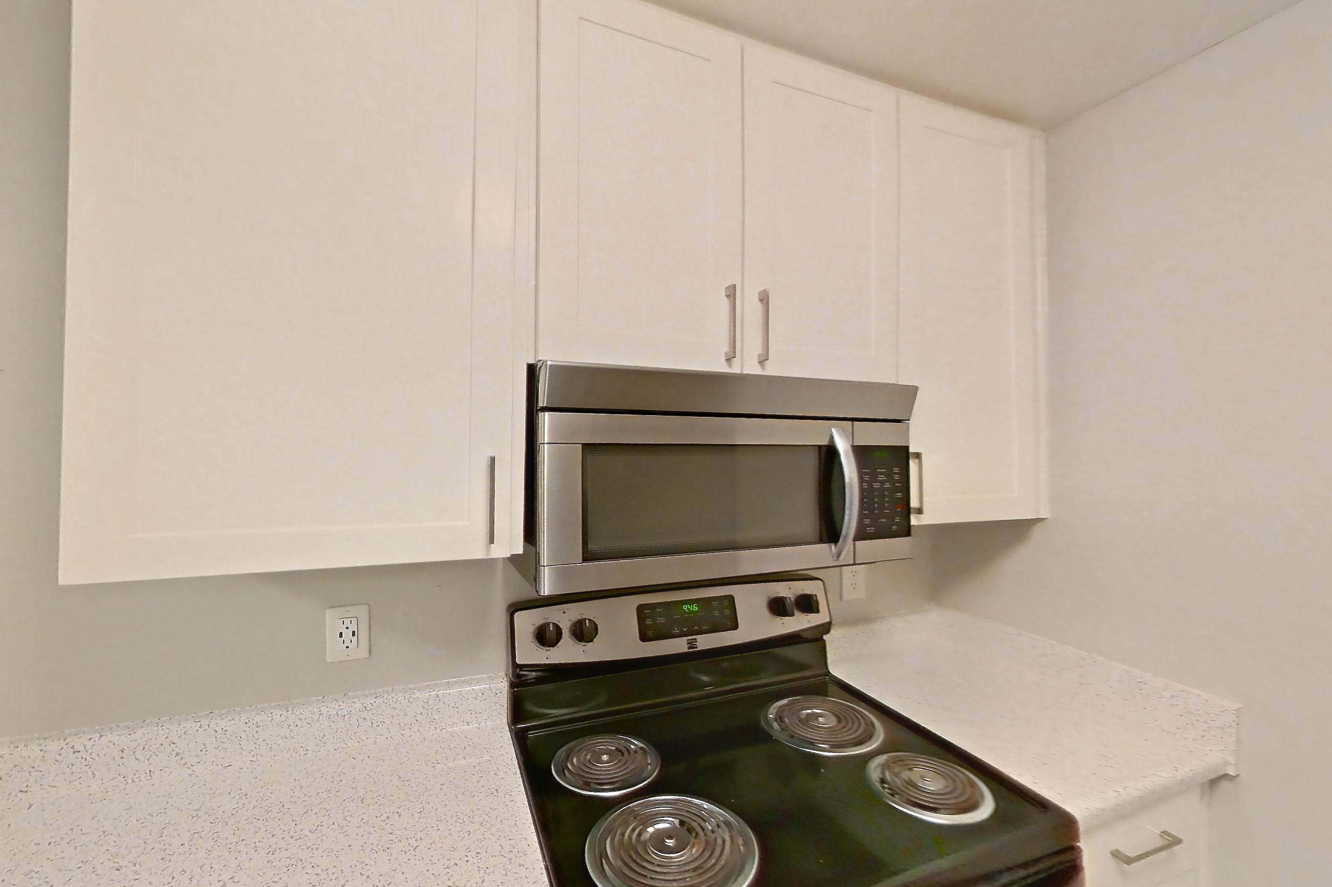 Kitchen with dishwasher, electric range, light stone countertops, light wood-finish flooring, microwave, oven/range, and stainless steel appliances, Apartment 11-04 at Avana Rancho Cucamonga