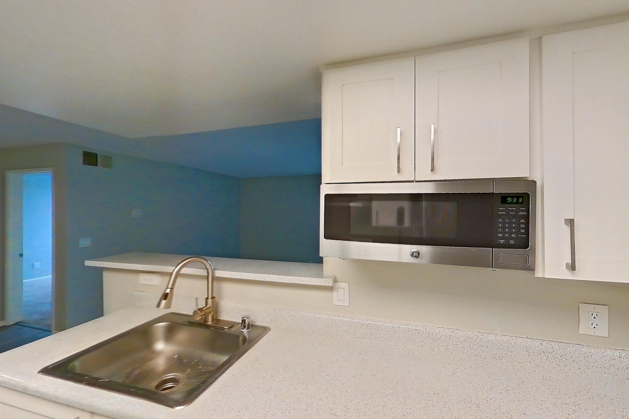 Kitchen with dishwasher, electric range, in-unit laundry, light countertops, light stone countertops, light wood-finish flooring, oven/range, refrigerator, and stainless steel appliances, Apartment 11 at Avana Rancho Cucamonga