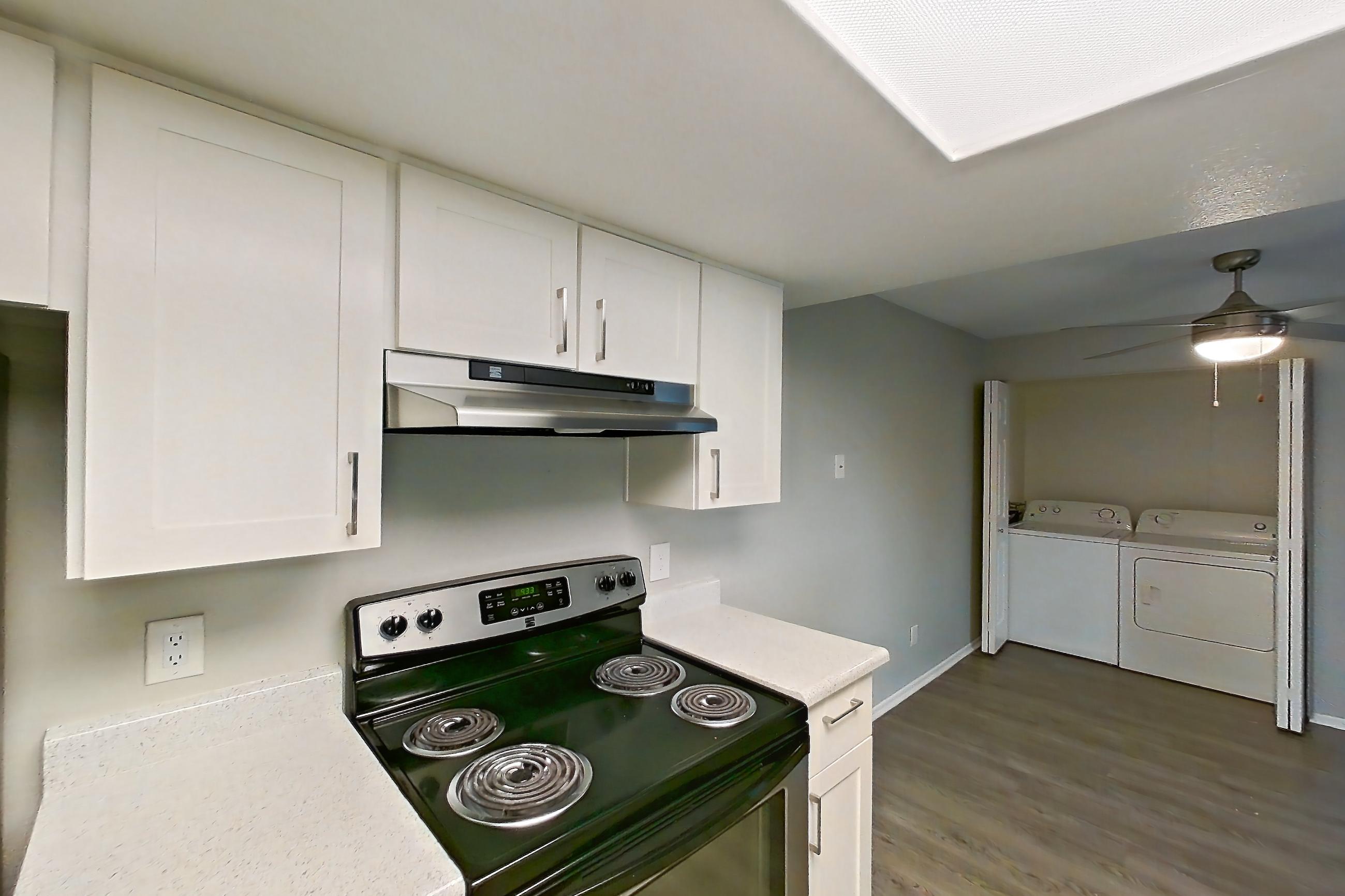 Kitchen with dishwasher, electric range, in-unit laundry, light countertops, light stone countertops, light wood-finish flooring, oven/range, refrigerator, and stainless steel appliances, Apartment 11 at Avana Rancho Cucamonga