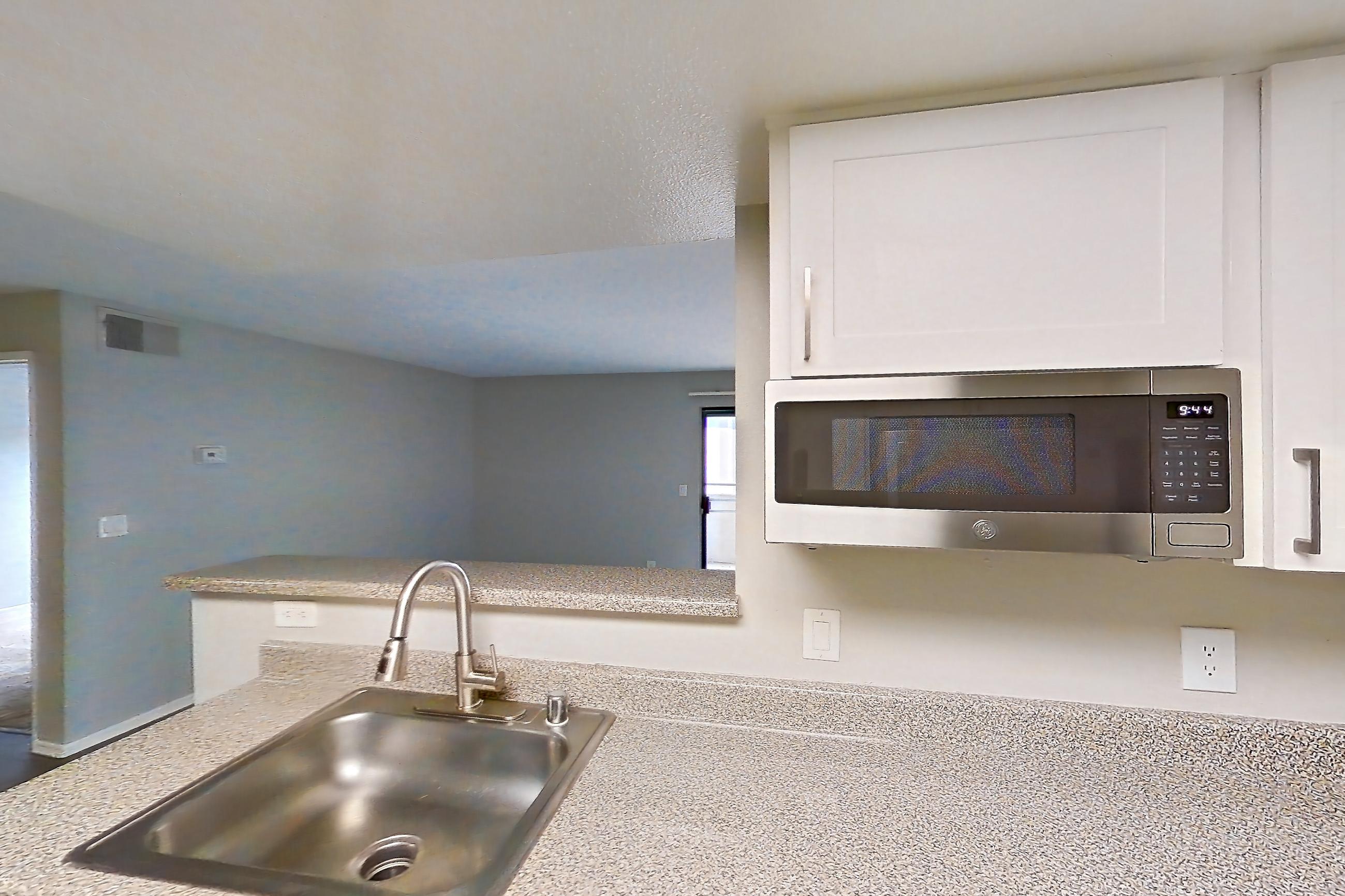 Kitchen with dark wood-finish flooring, dishwasher, electric range, in-unit laundry, light countertops, light stone countertops, light wood-finish flooring, oven/range, range hood, refrigerator, and stainless steel appliances, Apartment 18 at Avana Rancho Cucamonga