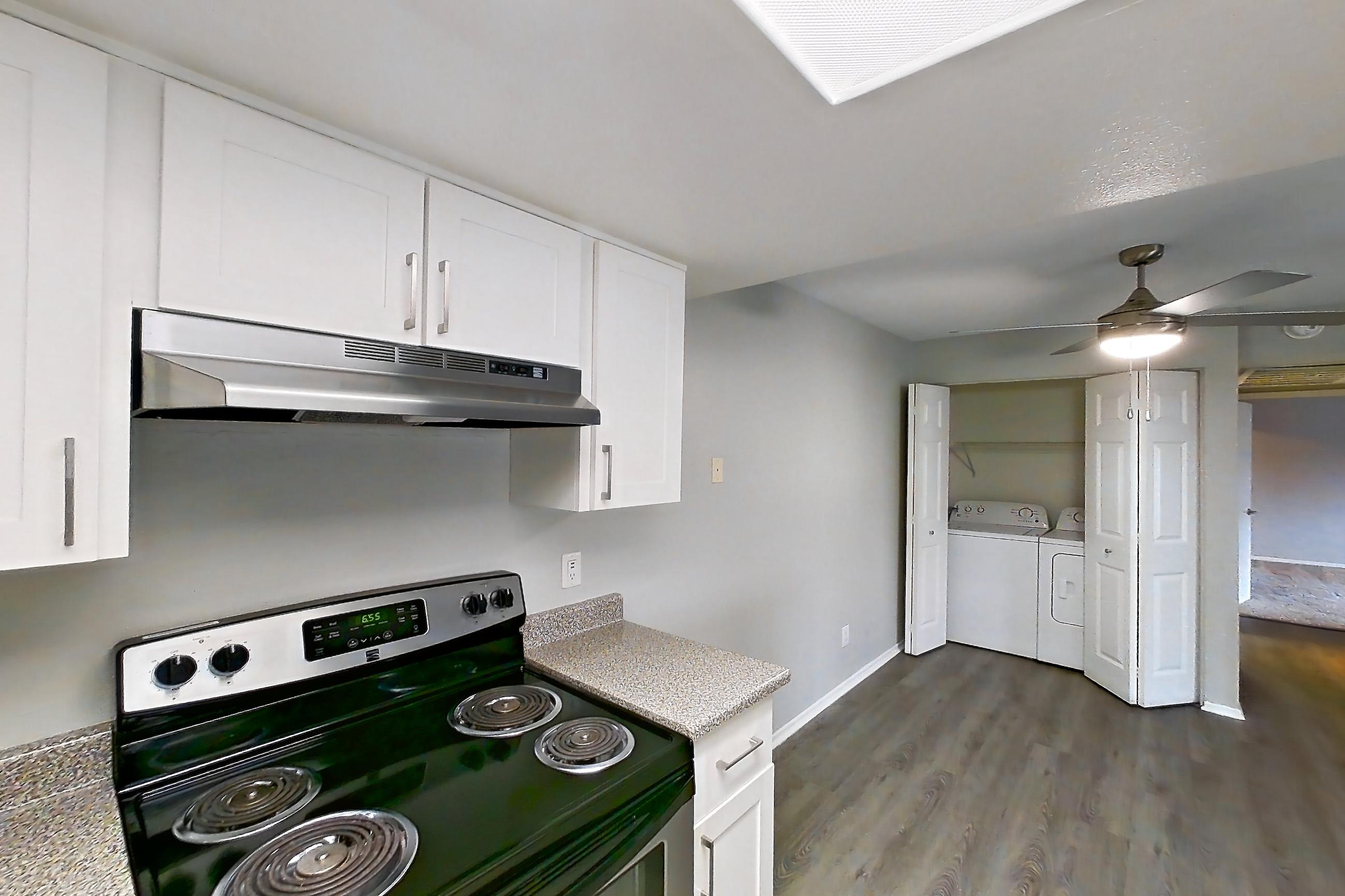 Kitchen with dark wood-finish flooring, dishwasher, electric range, in-unit laundry, light countertops, light stone countertops, light wood-finish flooring, oven/range, range hood, refrigerator, and stainless steel appliances, Apartment 18 at Avana Rancho Cucamonga