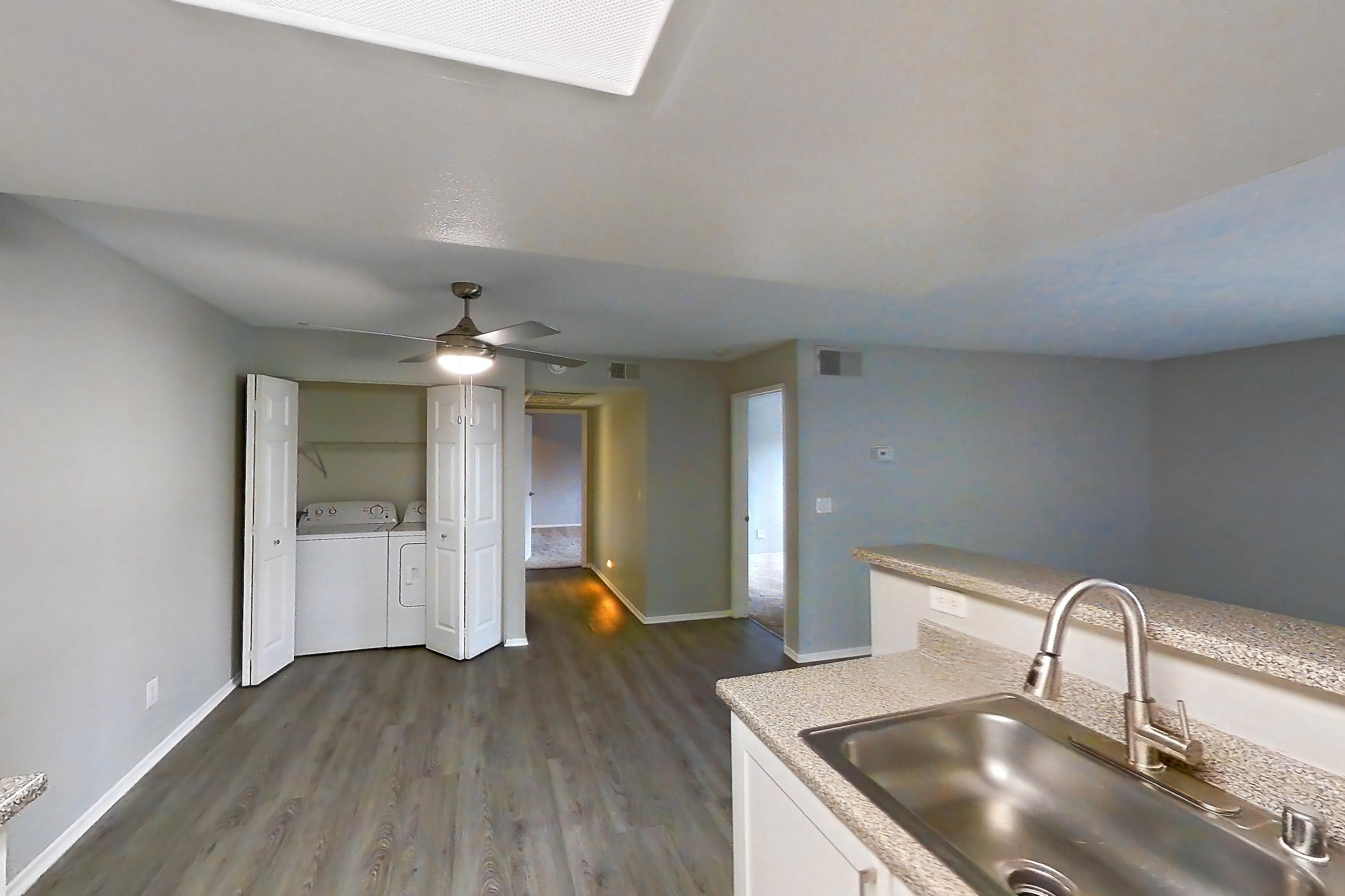 Kitchen with dark wood-finish flooring, dishwasher, electric range, in-unit laundry, light countertops, light stone countertops, light wood-finish flooring, oven/range, range hood, refrigerator, and stainless steel appliances, Apartment 18 at Avana Rancho Cucamonga