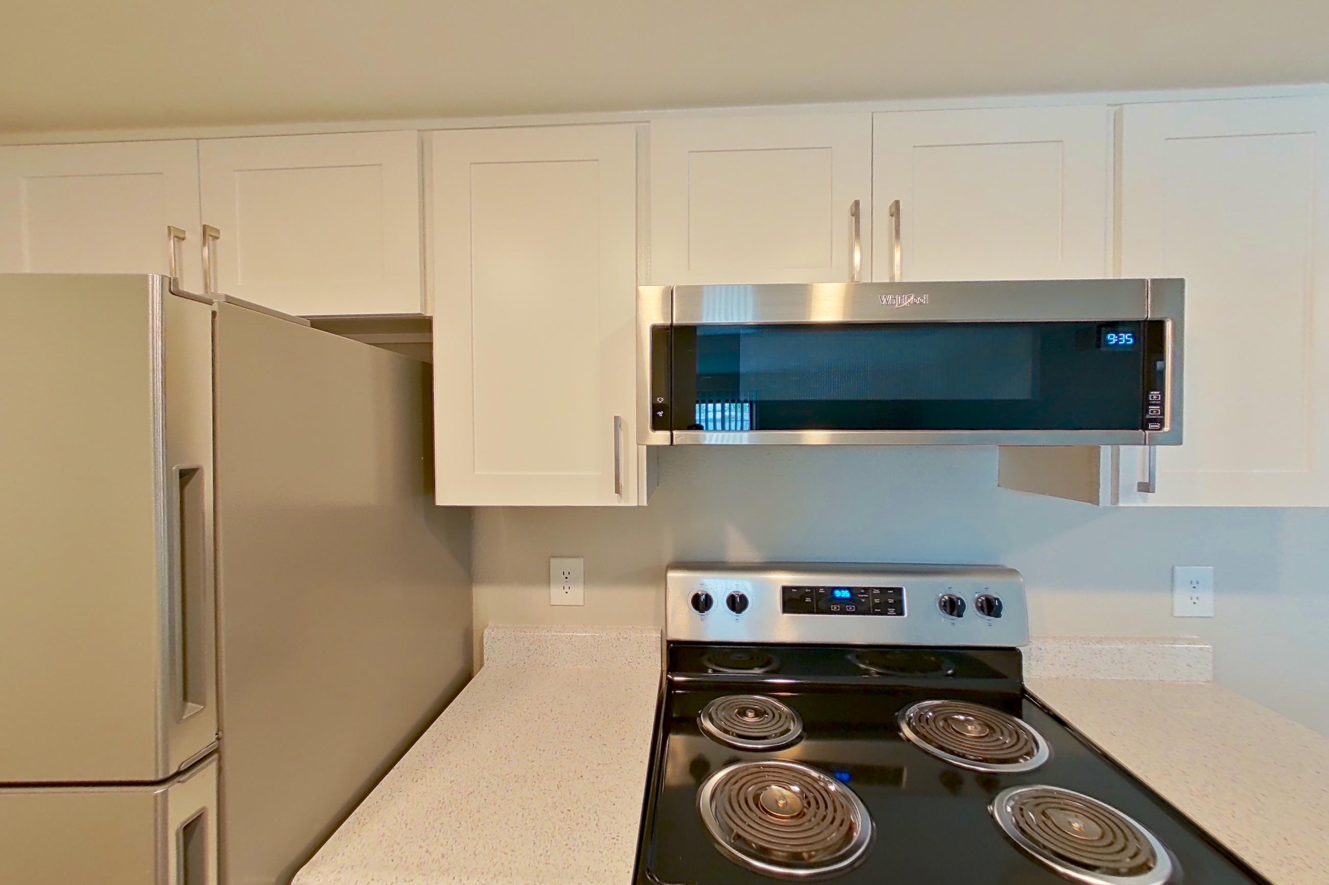 Kitchen with dishwasher, electric range, light countertops, light stone countertops, light wood-finish flooring, microwave, oven/range, refrigerator, stainless steel appliances, and white appliances, Apartment 22 at Avana Rancho Cucamonga