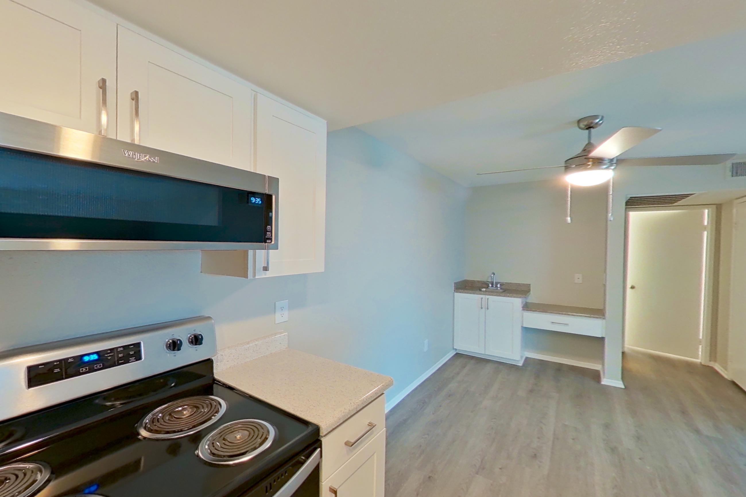 Kitchen with dishwasher, electric range, light countertops, light stone countertops, light wood-finish flooring, microwave, oven/range, refrigerator, stainless steel appliances, and white appliances, Apartment 22 at Avana Rancho Cucamonga