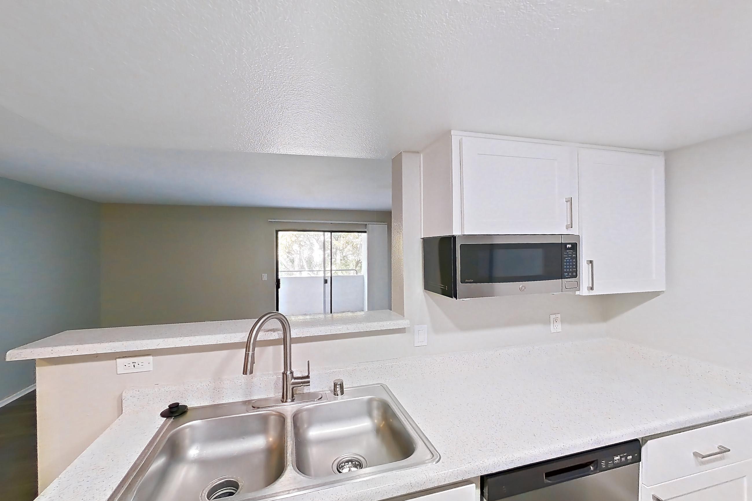 Kitchen with dishwasher, electric range, in-unit laundry, light countertops, light stone countertops, light wood-finish flooring, oven/range, refrigerator, and stainless steel appliances, Apartment 23 at Avana Rancho Cucamonga