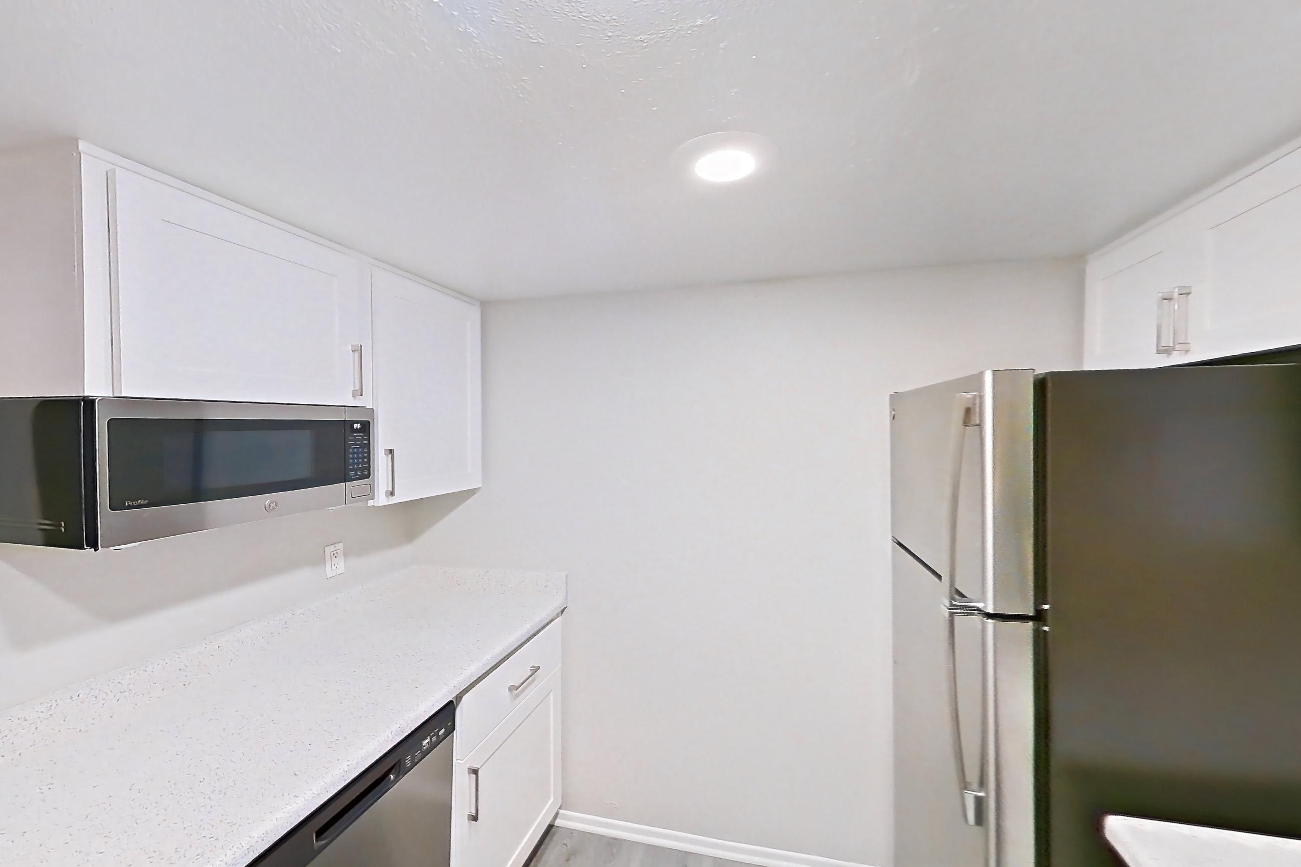 Kitchen with dishwasher, electric range, in-unit laundry, light countertops, light stone countertops, light wood-finish flooring, oven/range, refrigerator, and stainless steel appliances, Apartment 23 at Avana Rancho Cucamonga