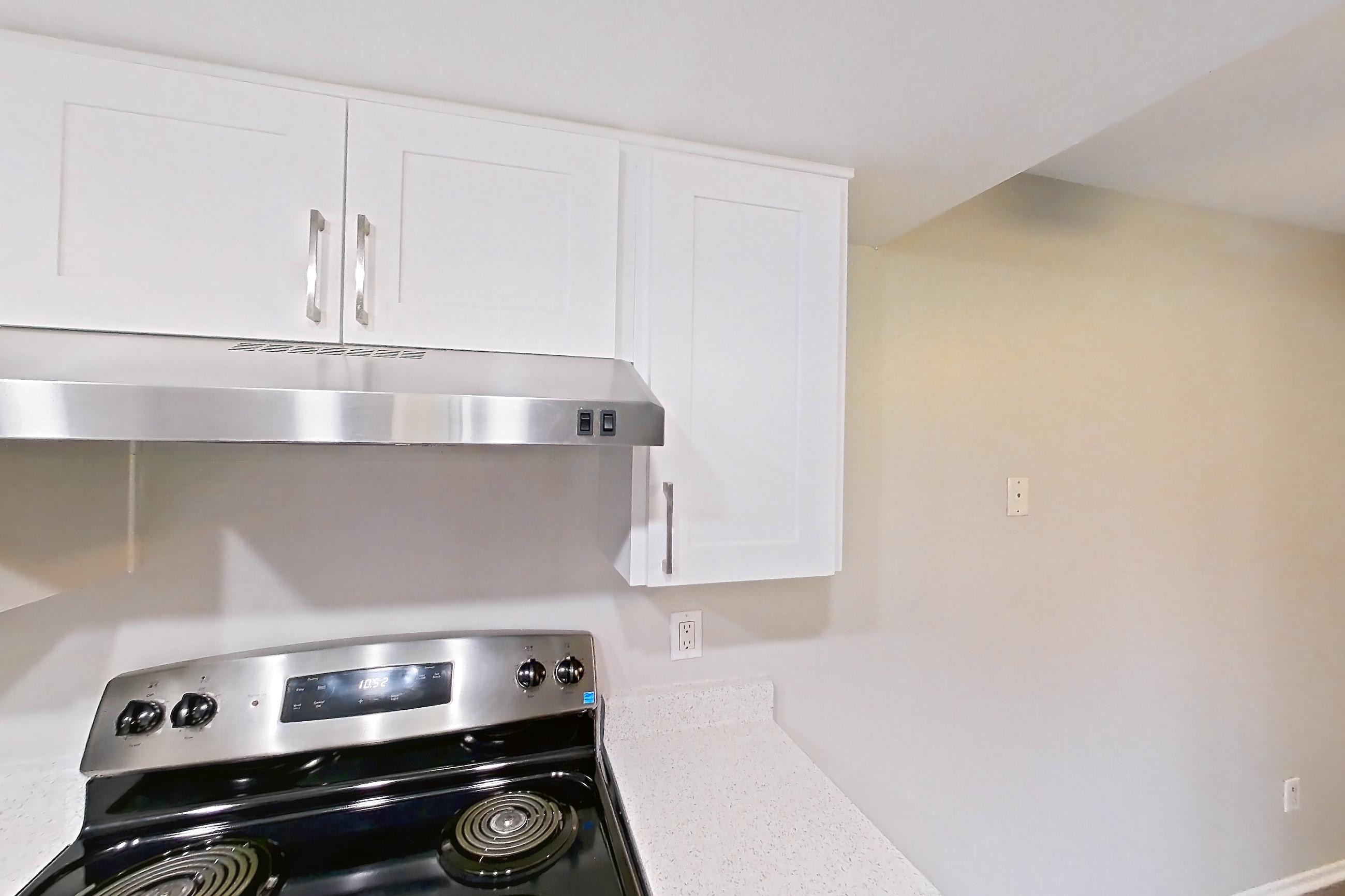 Kitchen with dishwasher, electric range, in-unit laundry, light countertops, light stone countertops, light wood-finish flooring, oven/range, refrigerator, and stainless steel appliances, Apartment 23 at Avana Rancho Cucamonga