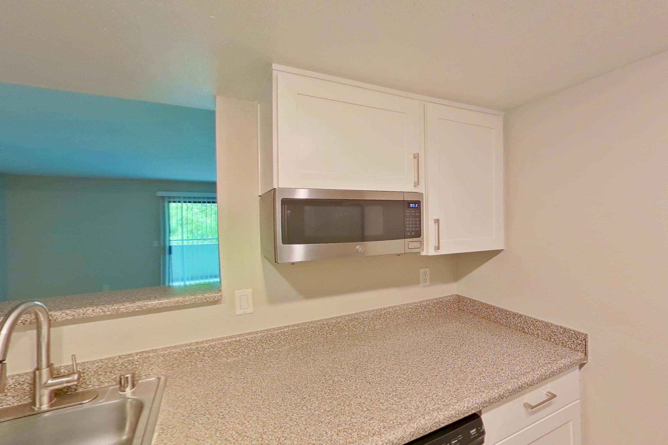 Kitchen with dishwasher, electric range, light countertops, light stone countertops, light wood-finish flooring, oven/range, range hood, refrigerator, and stainless steel appliances, Apartment 11 at Avana Rancho Cucamonga