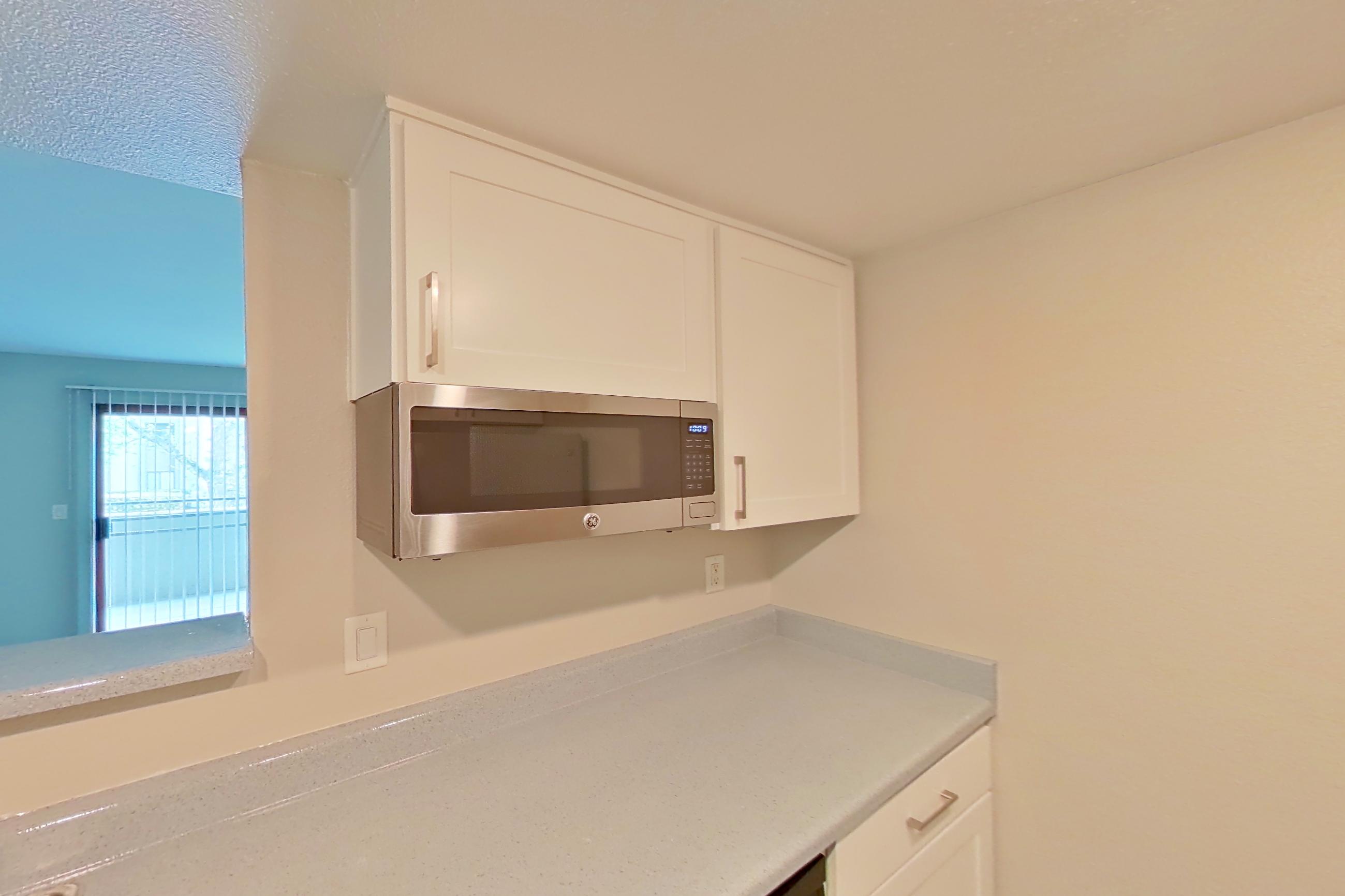Kitchen with dishwasher, electric range, light countertops, light stone countertops, light wood-finish flooring, oven/range, range hood, refrigerator, and stainless steel appliances, Apartment 06 at Avana Rancho Cucamonga